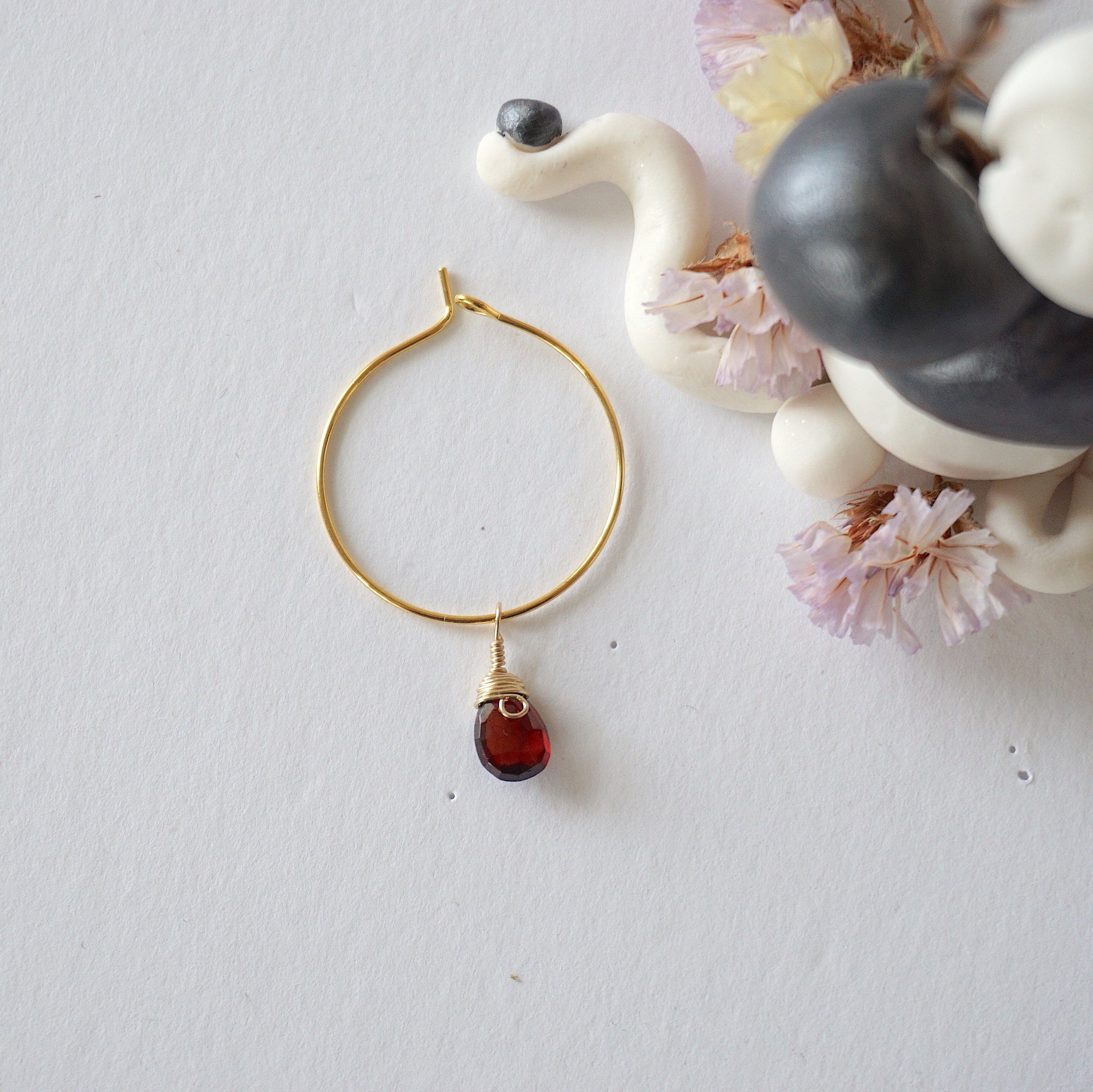 Flat lay of a gold plated garnet hoop drop earring, highlighting the wire wrapped natural garnet gemstone and minimalist hoop design