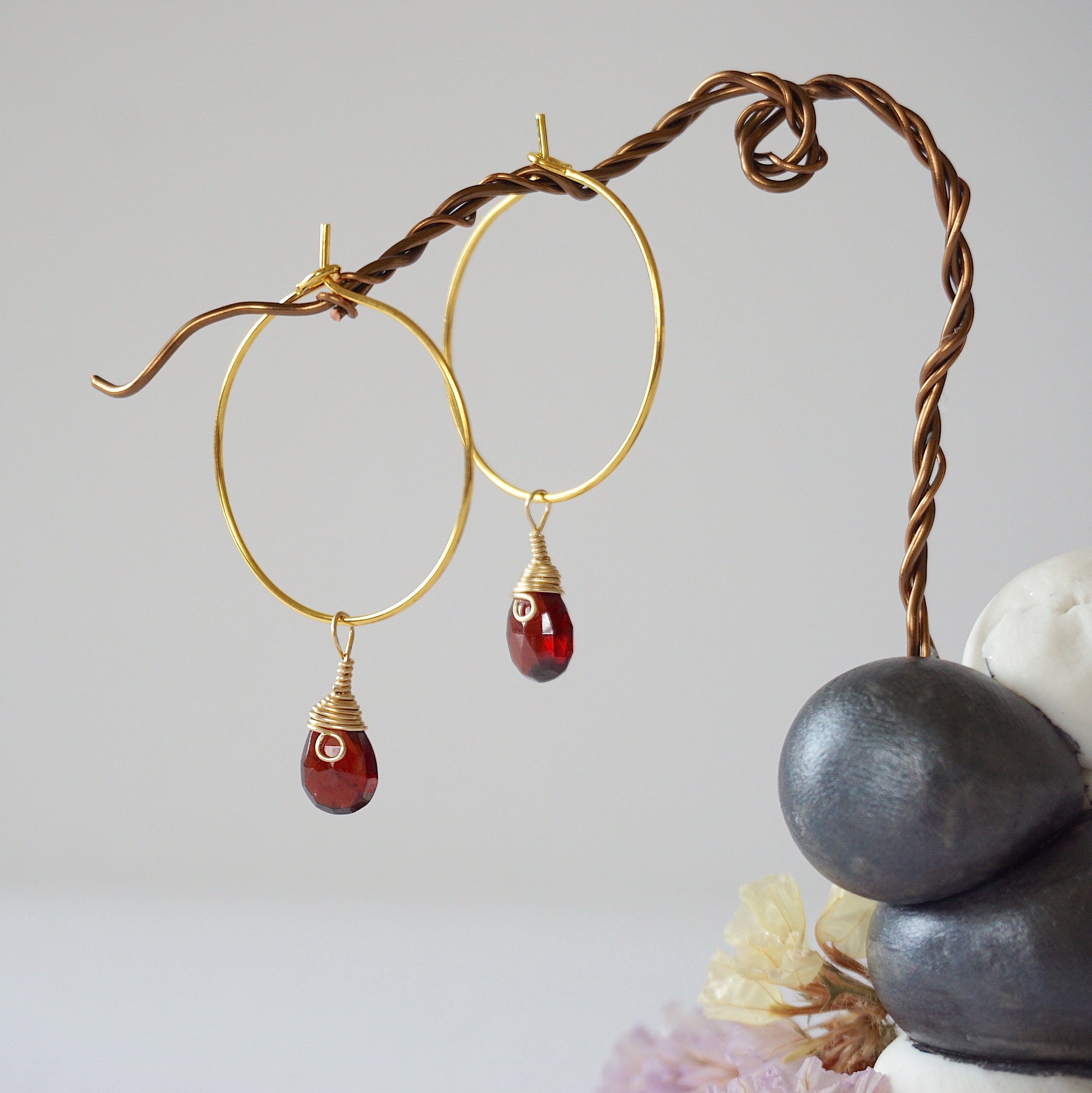 Close-up of handcrafted garnet hoop drop earrings in gold plated brass, featuring wire wrapped natural red garnet gemstones on a jewelry display