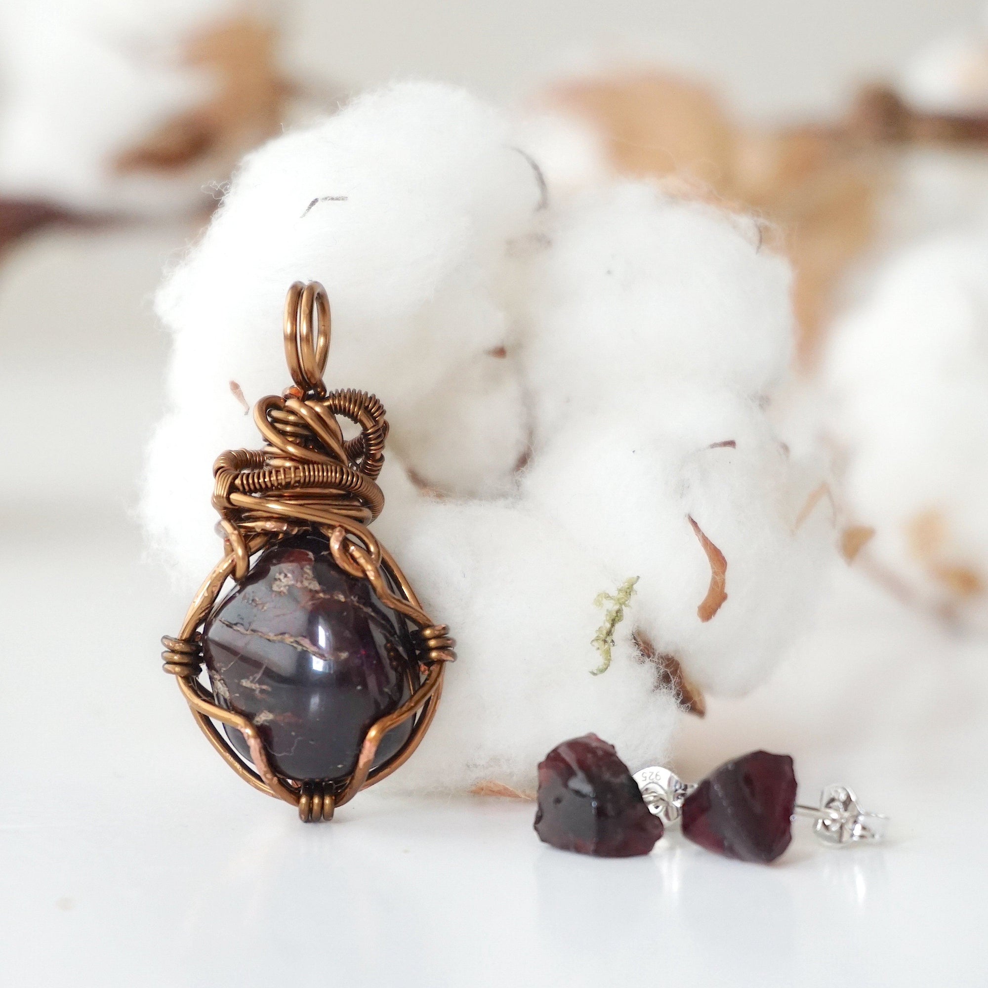 Back view of a wire wrapped garnet pendant and side view of garnet stud earrings in a women’s jewelry set