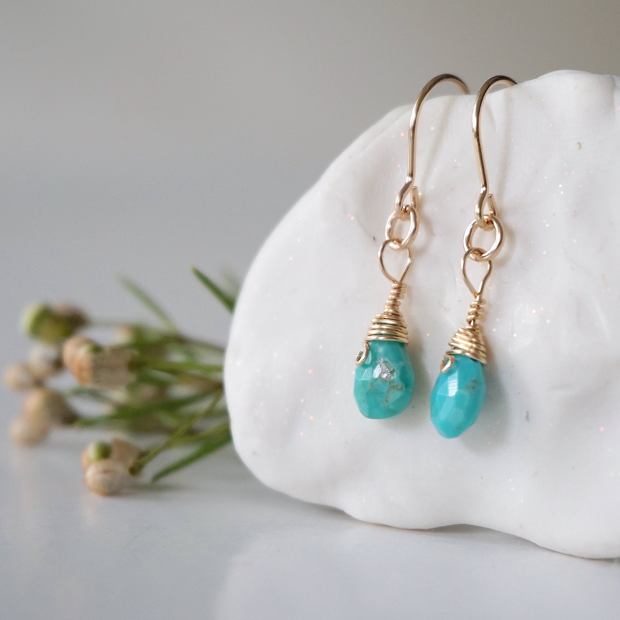 Left side angle of gold turquoise dangle earrings displaying handmade wire wrapped design and natural stone variation