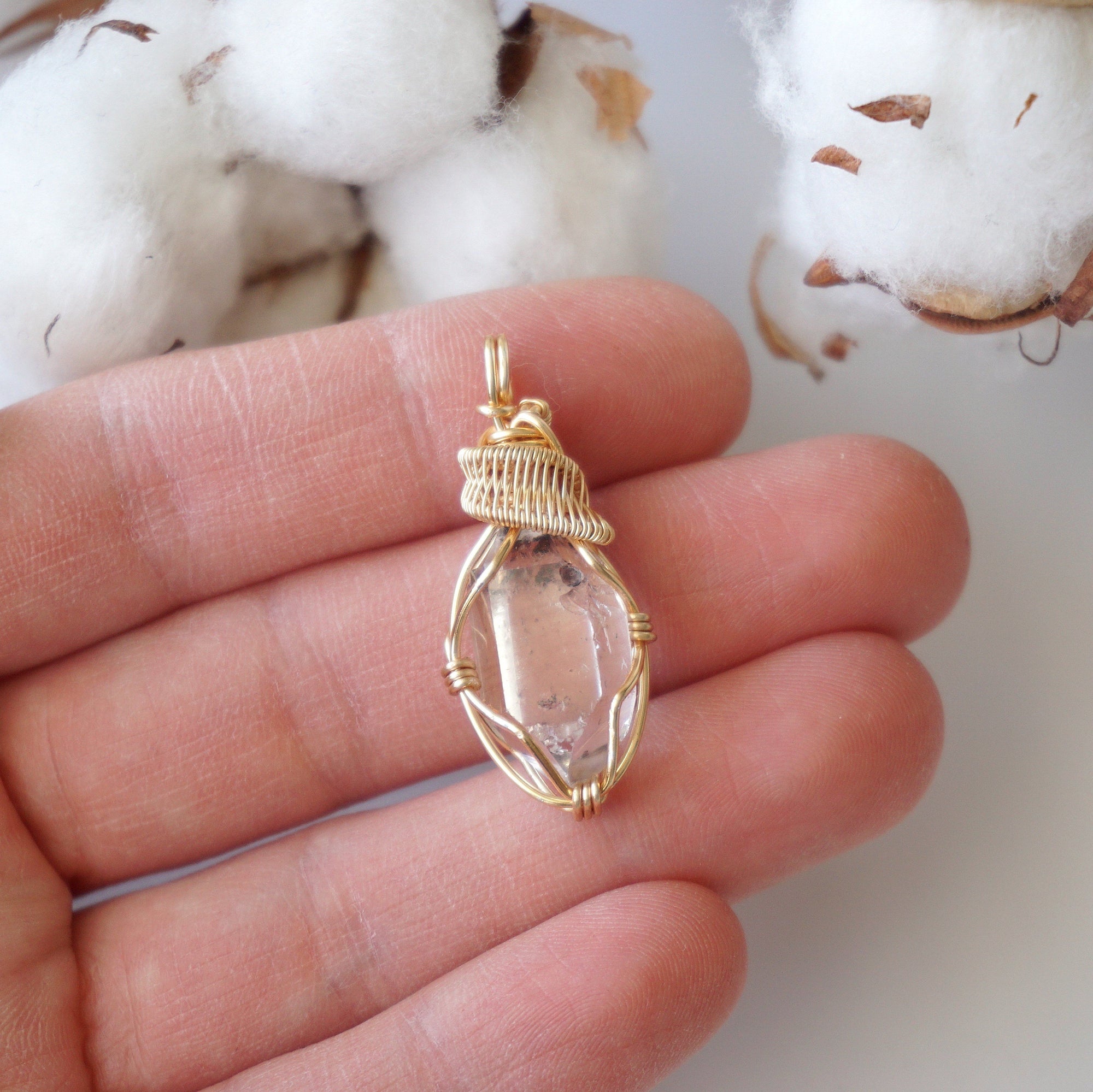 Raw Herkimer diamond pendant shown in hand for size reference, handmade in warm gold copper wire.