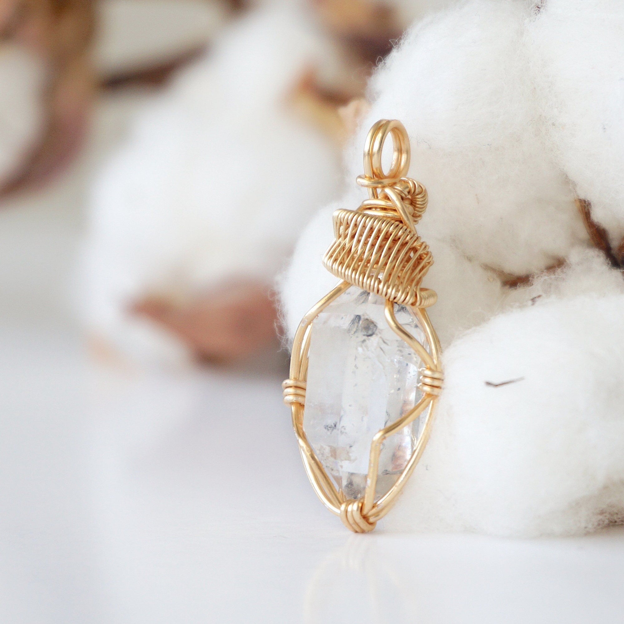 Left angle view of handmade Herkimer diamond pendant highlighting warm gold copper wire artistry.