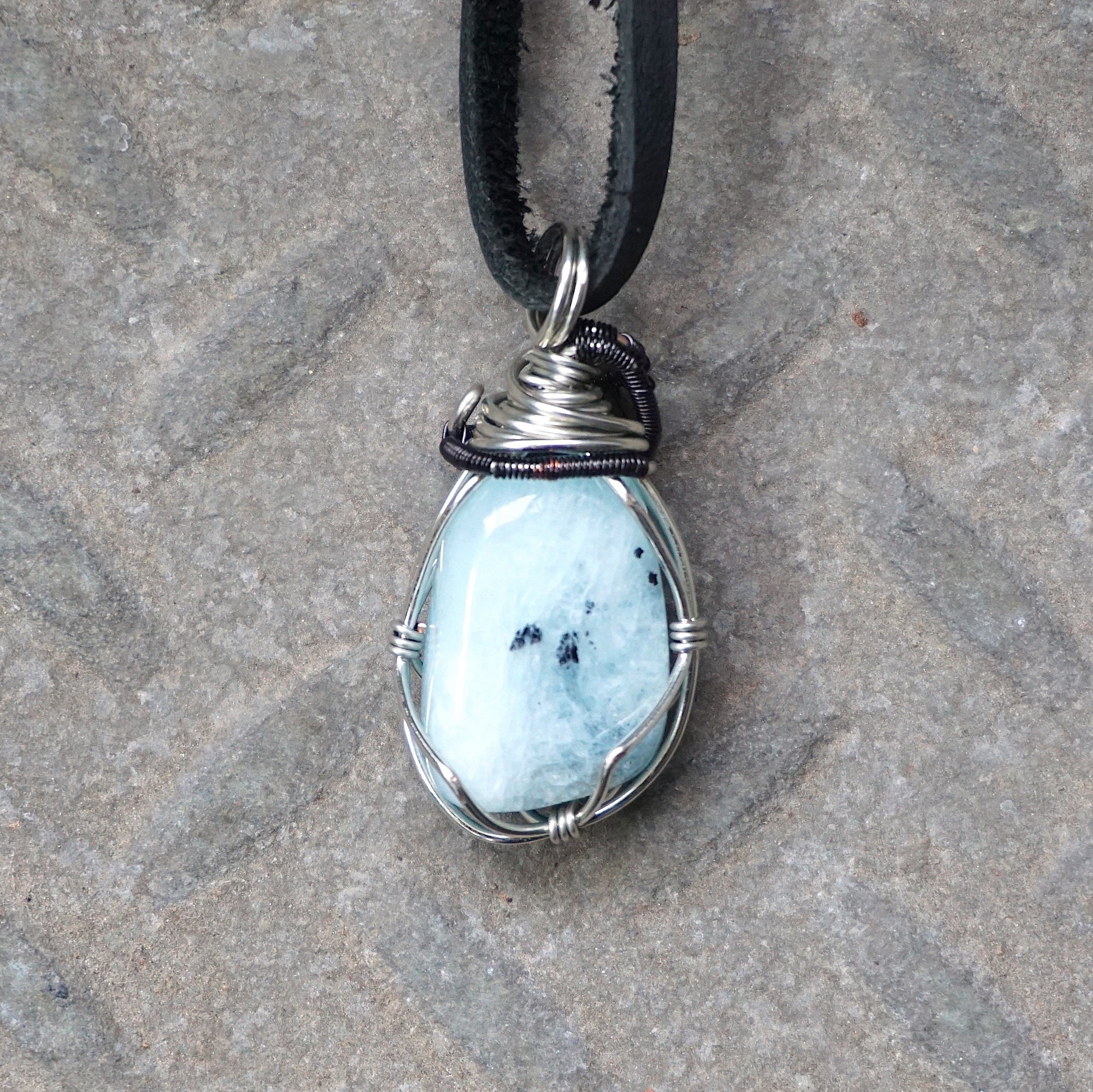 Back angle of men's aquamarine pendant on a black leather cord, highlighting wire wrapped setting and natural stone texture, black and white gold finish