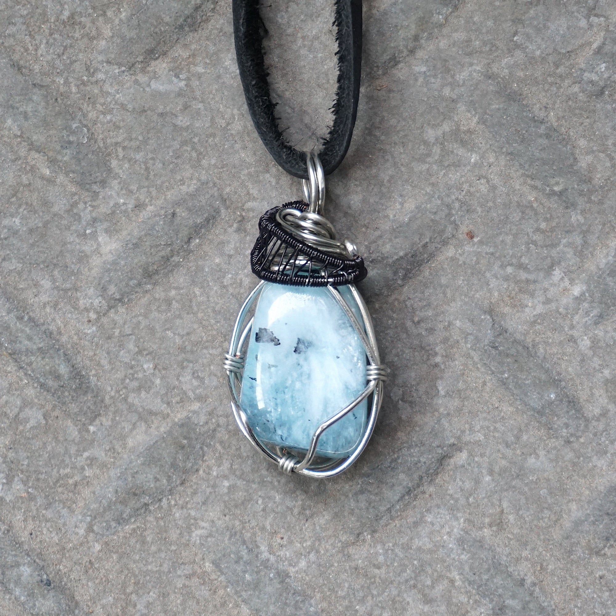Detailed front angle of men's aquamarine pendant on a black leather cord, artisan wire wrapped in black and white gold finish