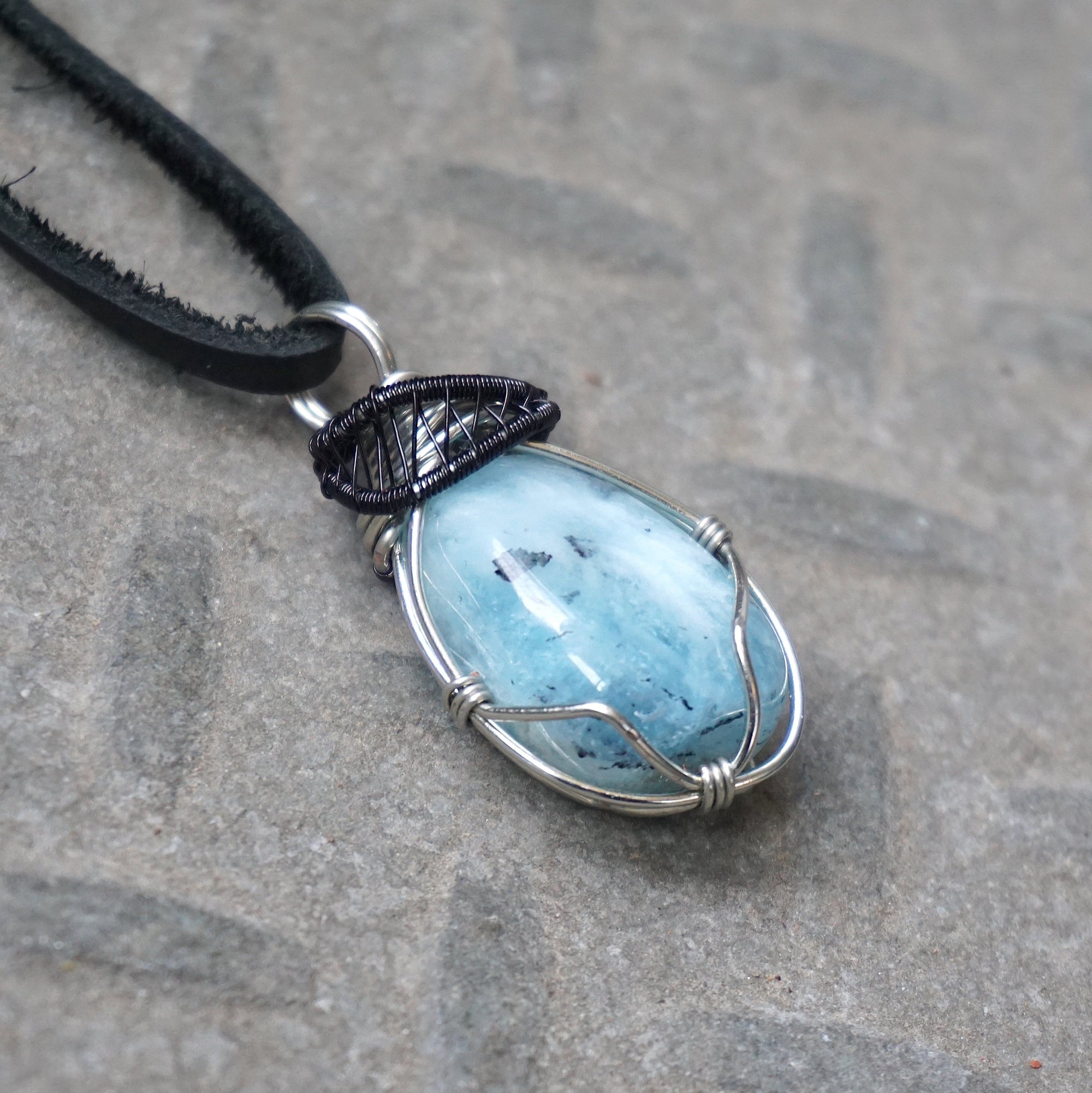Men's aquamarine pendant on a black leather cord, detailed side angle view with artisan wire wrapping in black and white gold finish, Designs by Nature Gems