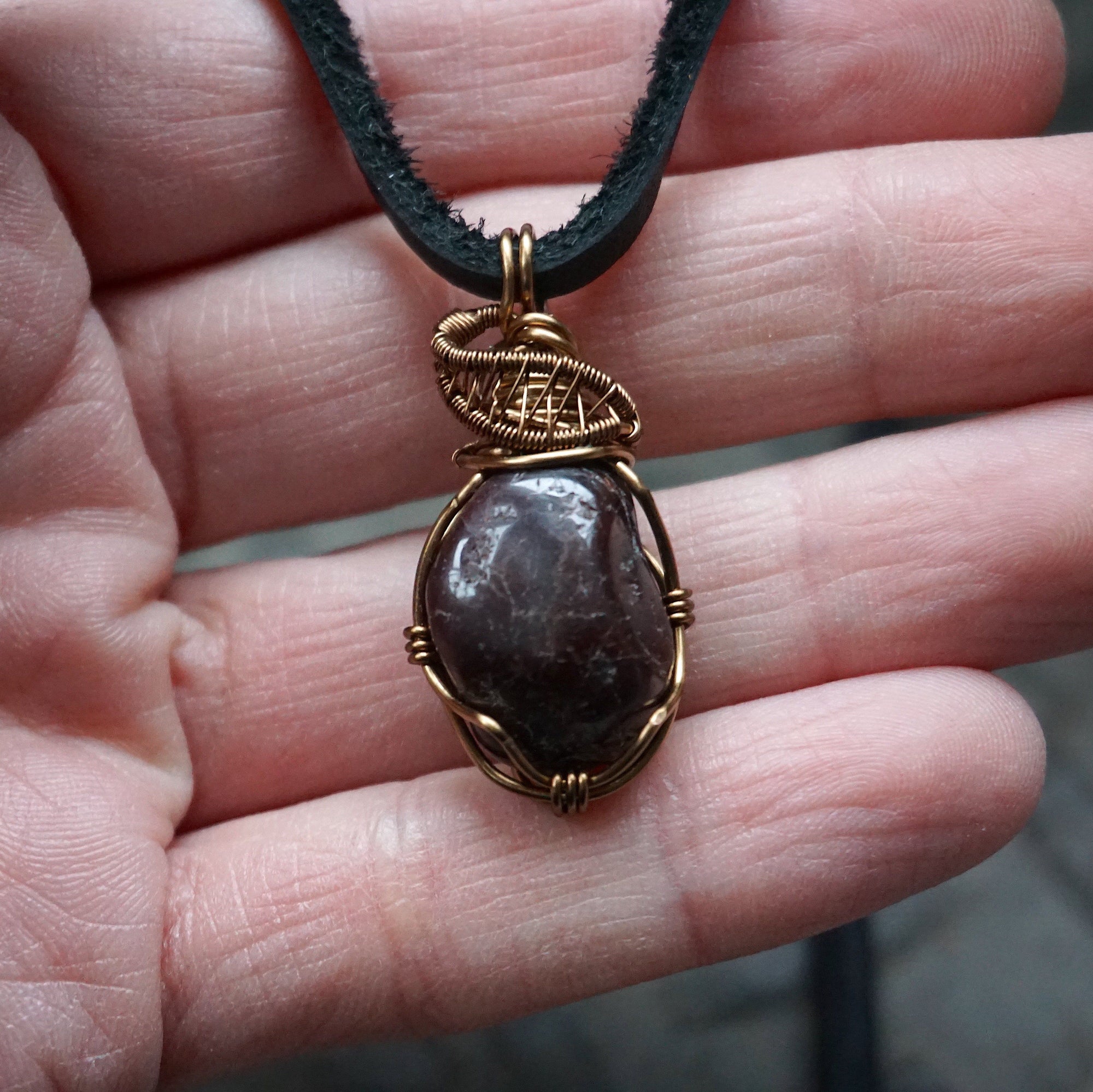 Men’s garnet pendant necklace in antique bronze copper held in hand for size reference, featuring a natural garnet on a black leather cord
