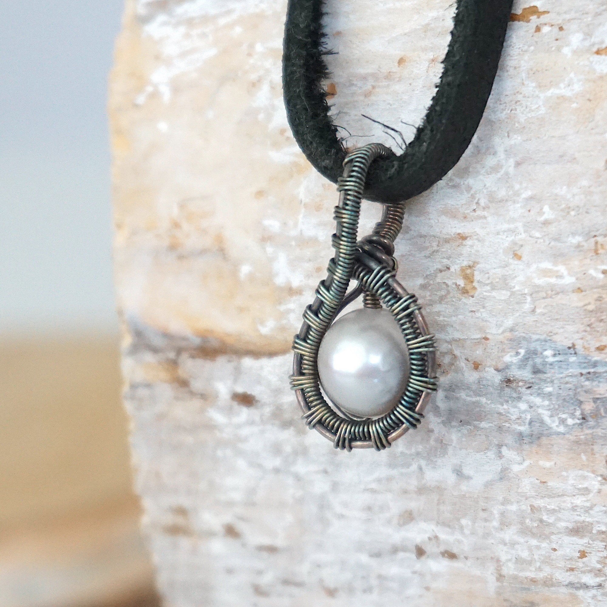 Side angle view of a men’s pearl pendant necklace wrapped in antiqued sterling silver on a black leather cord