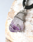 Left side angle of men’s raw amethyst pendant necklace on black leather cord, white gold plated copper wire wrap