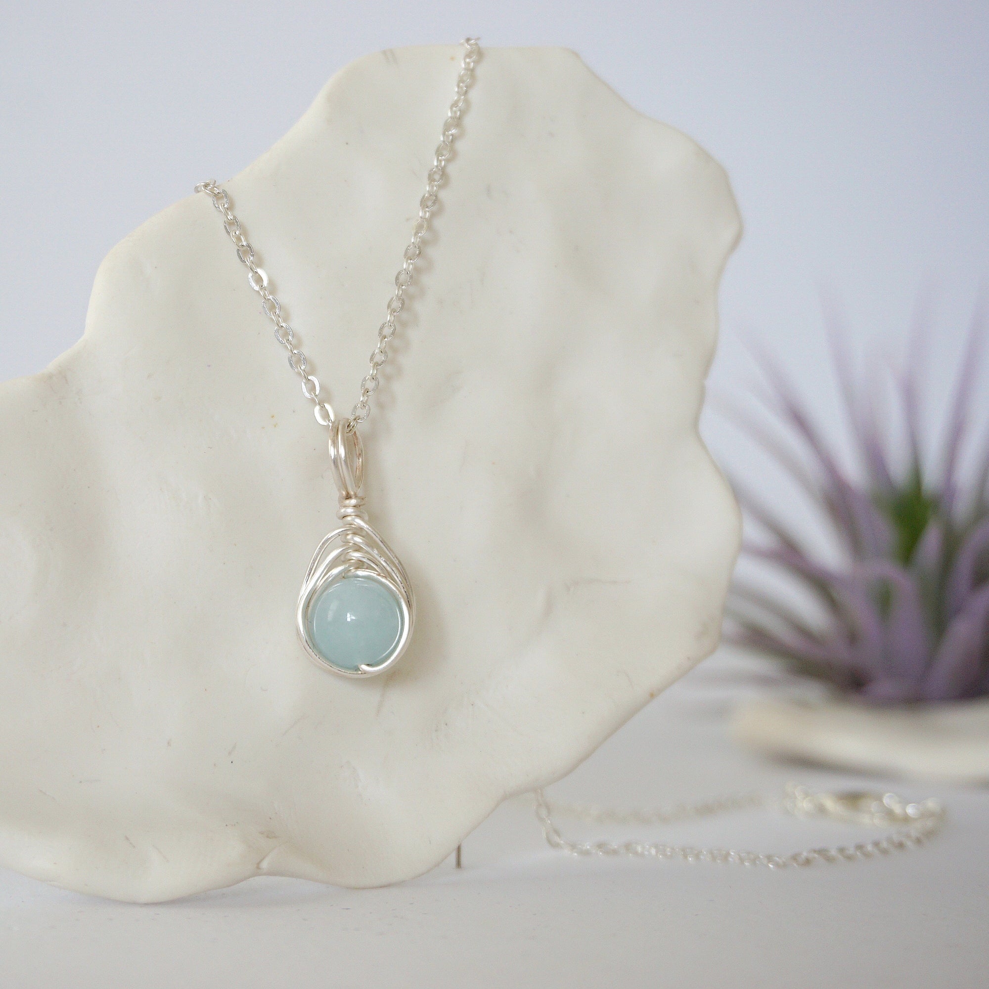 Zoomed in look at minimalist aquamarine necklace on display, artisan wire wrapped, soft silver finish, March birthstone