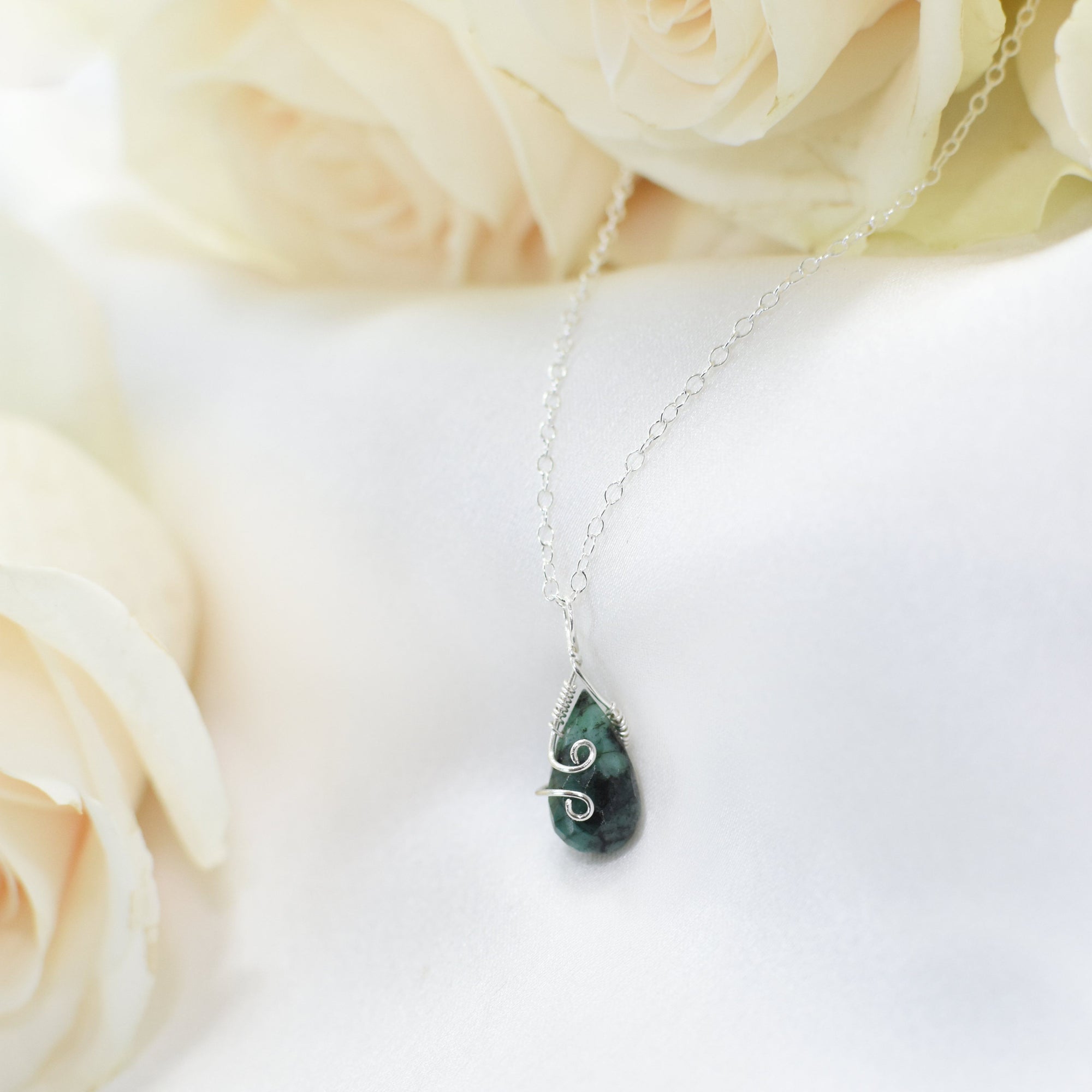 Detailed angle view of minimalist emerald necklace for women with faceted emerald and sterling silver wire wrapping