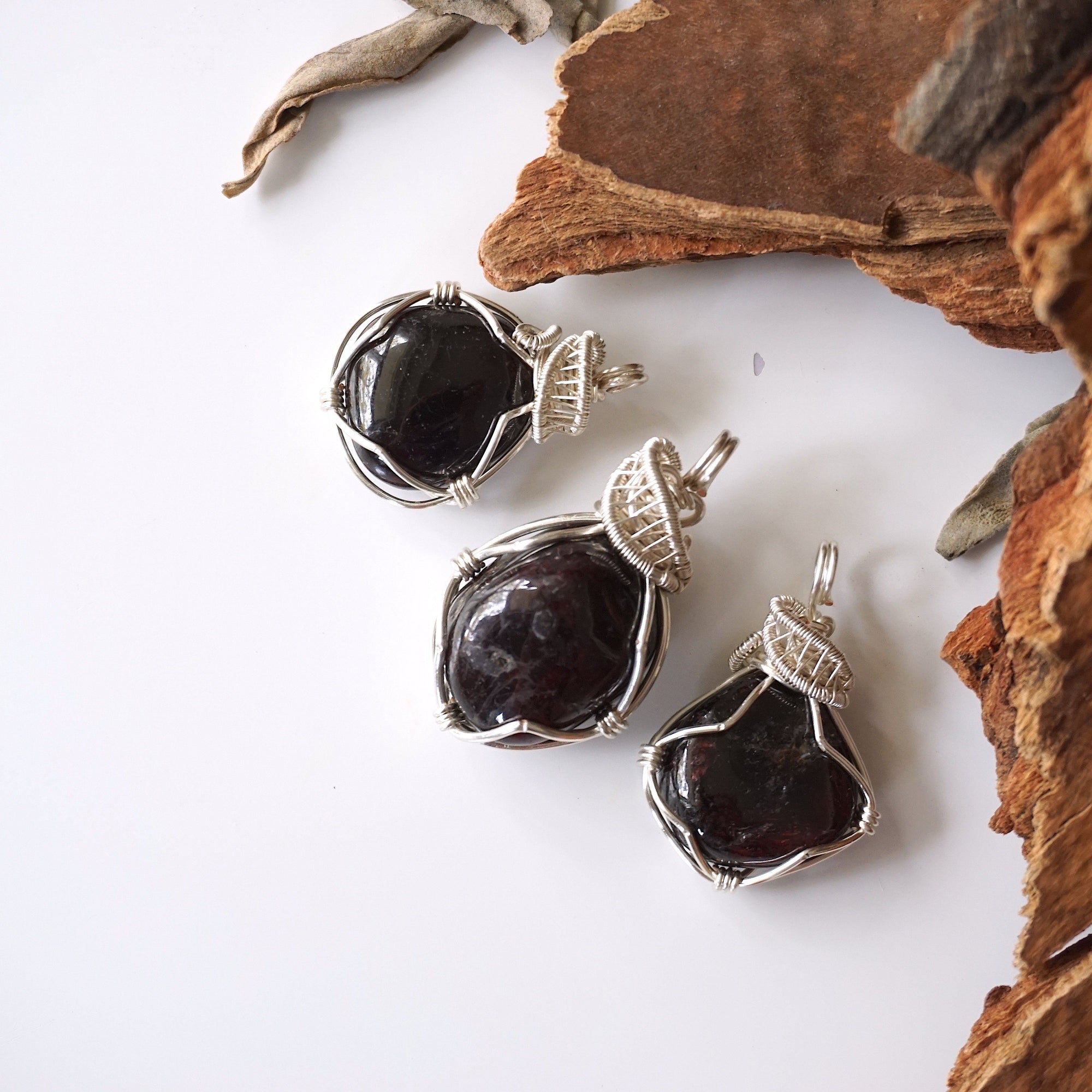 Three natural raw garnet pendants showing variation in size, shape, and deep red color tones