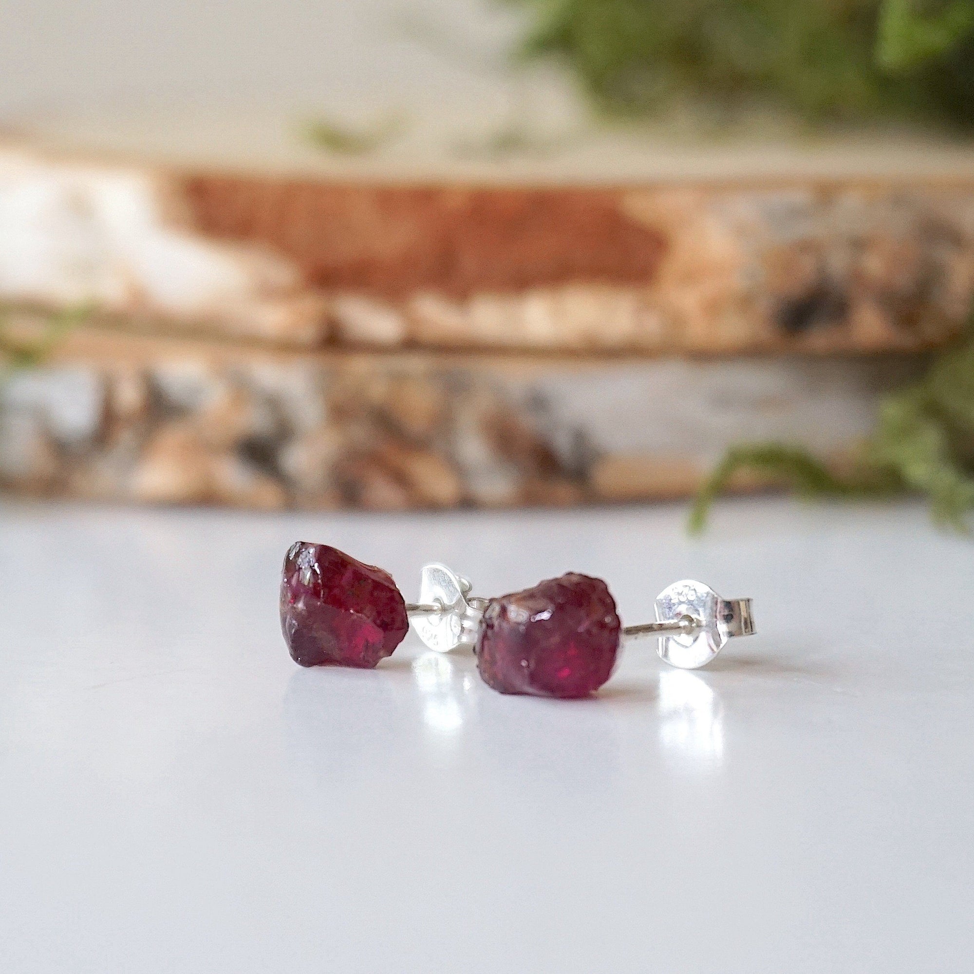 Side view of natural raw garnet stud earrings showing raw stone texture and sterling silver post setting