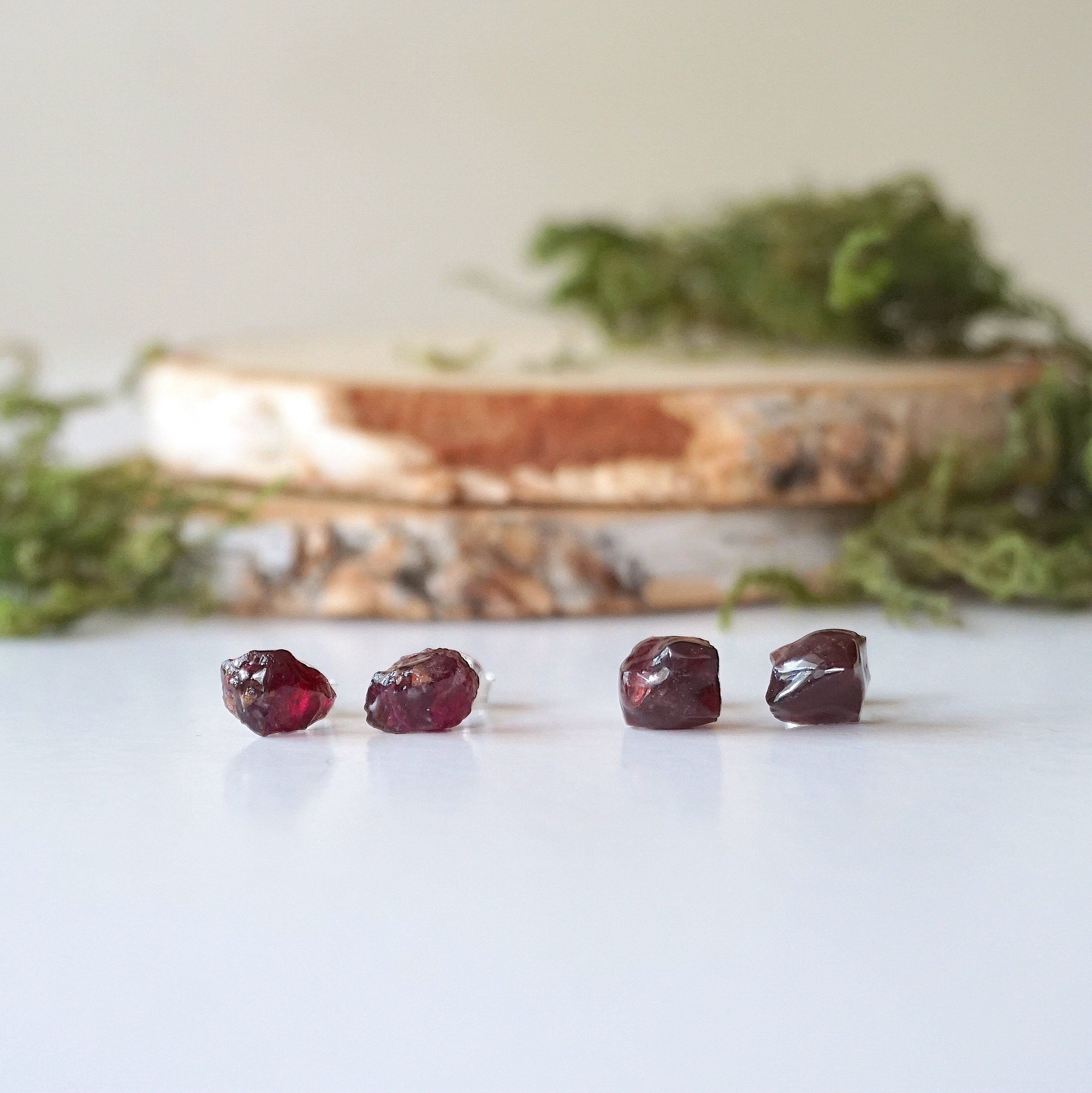 Two pairs of natural garnet stud earrings in sterling silver showing unique stone variation in size, shape, and deep red tone