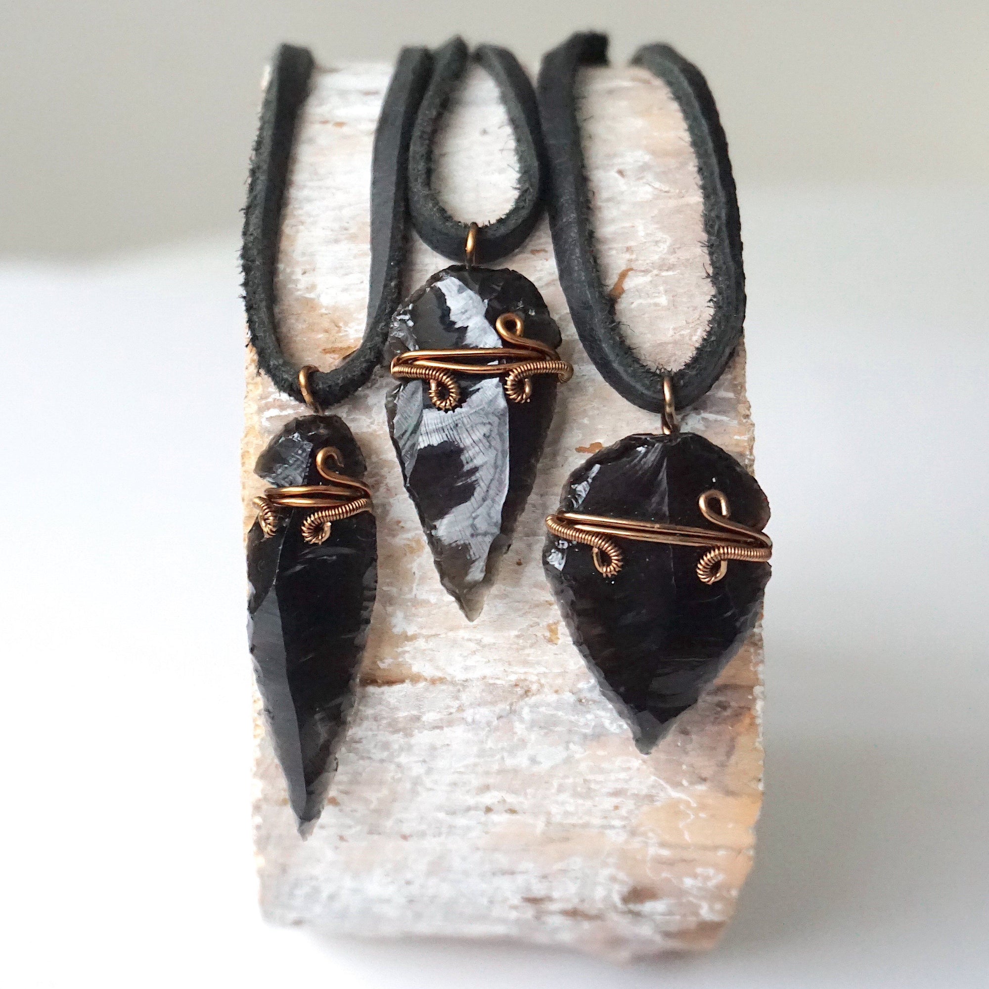 Three men’s black obsidian arrowhead pendants with antique bronze copper wire wrap, showing natural crystal variations, by Designs by Nature Gems.