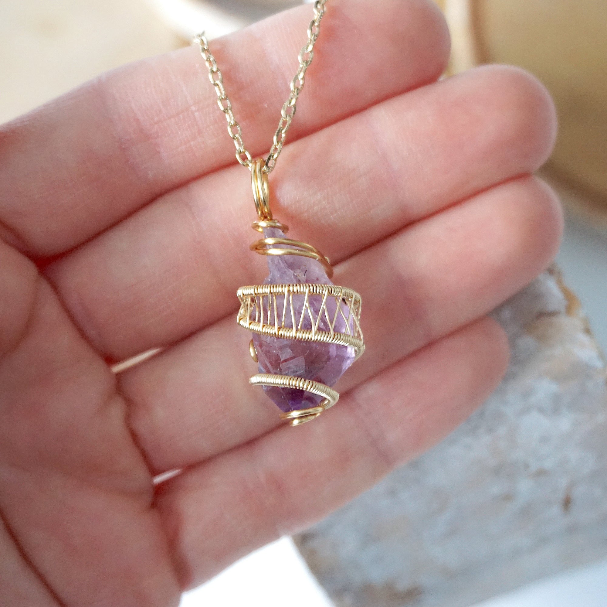 Raw amethyst point pendant necklace on gold plated brass chain held in hand for size reference