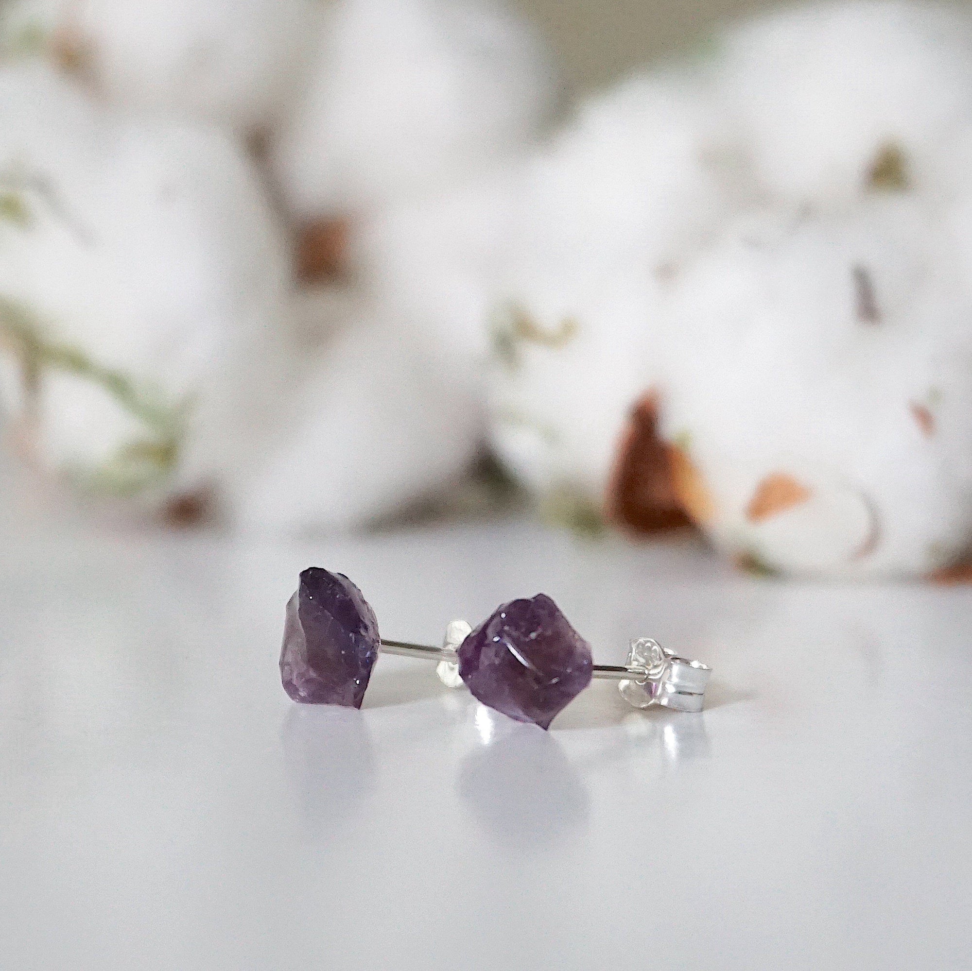 Side angle view of raw amethyst stud earrings, unpolished natural amethyst stones, sterling silver posts