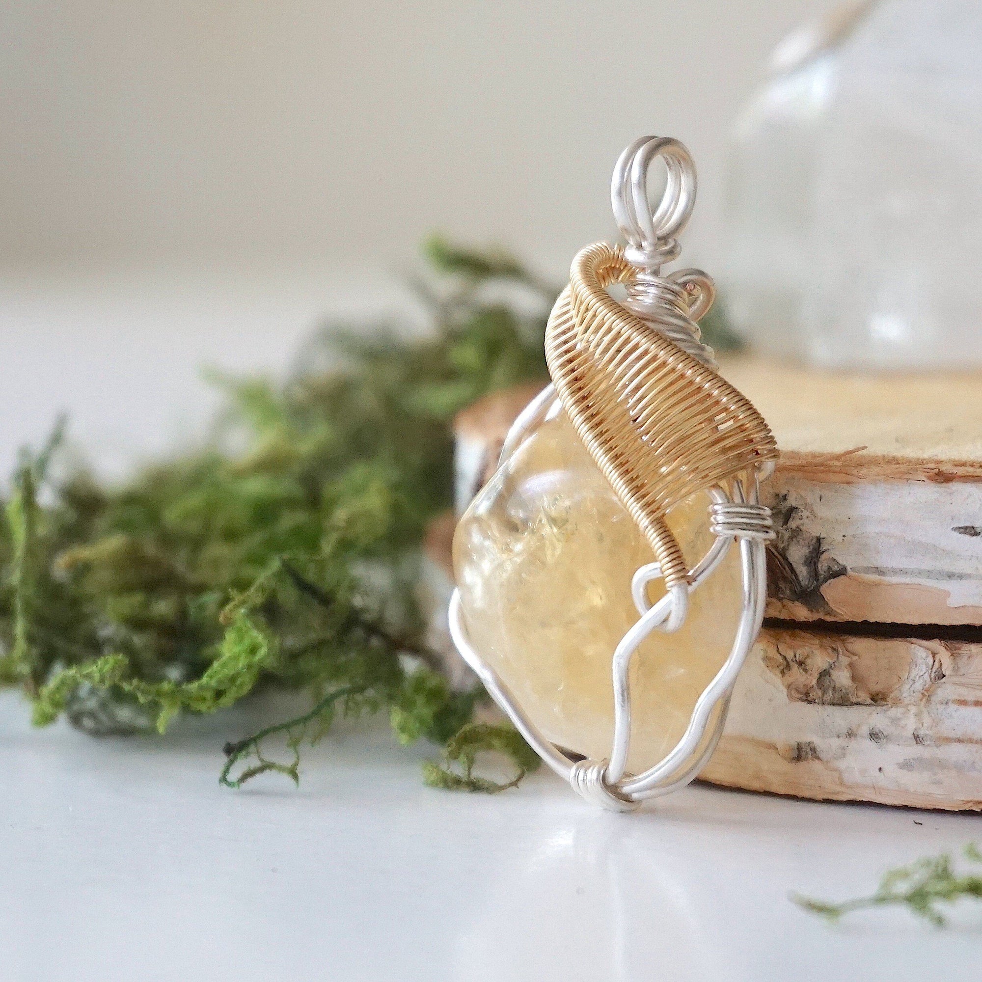 Close up of wire wrapped raw citrine crystal showing silver and gold plated copper craftsmanship and natural unpolished stone texture