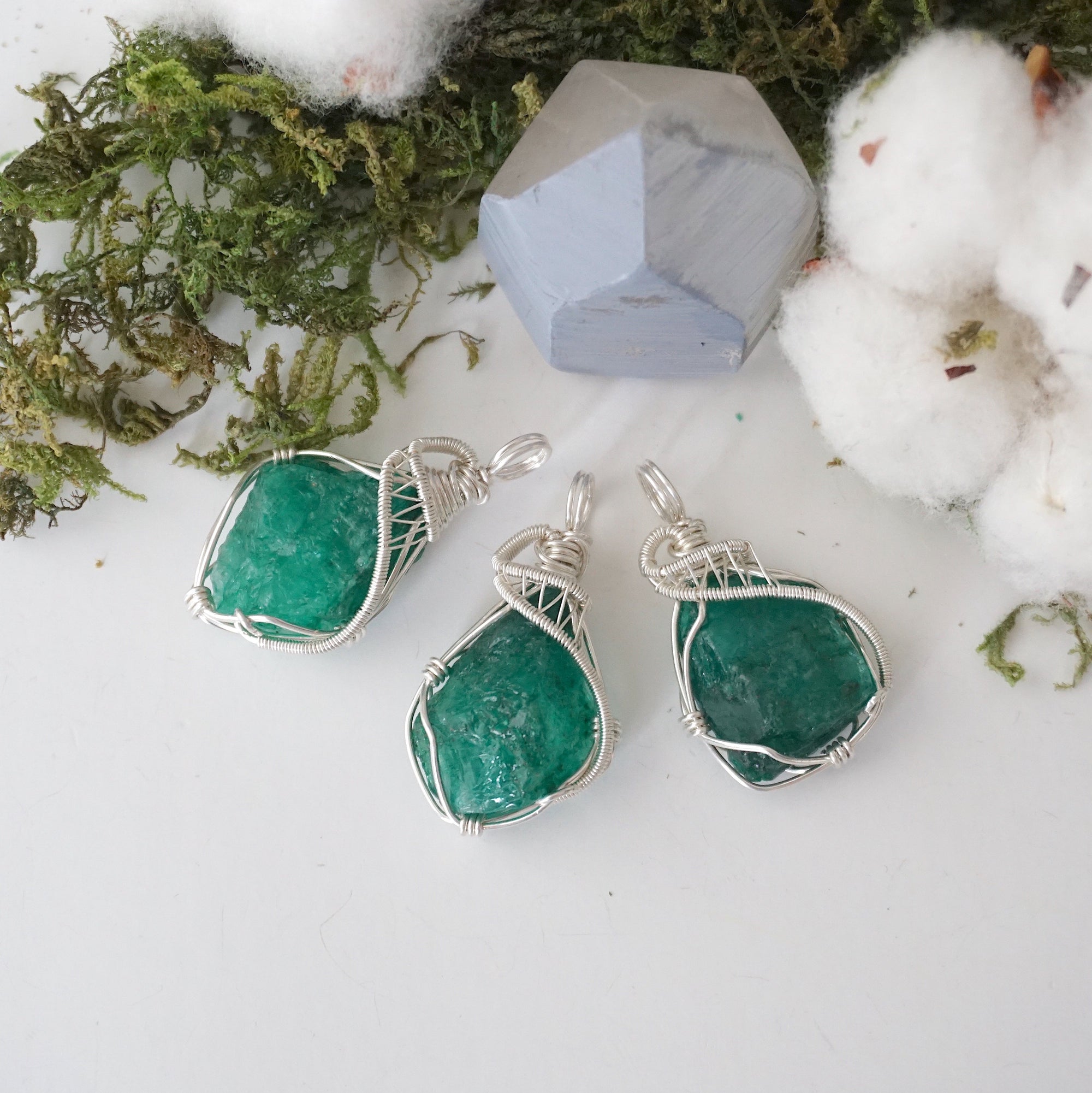 Three raw emerald pendants for women showing natural variation in emerald size, shape, and green colour in sterling silver wire wrapping