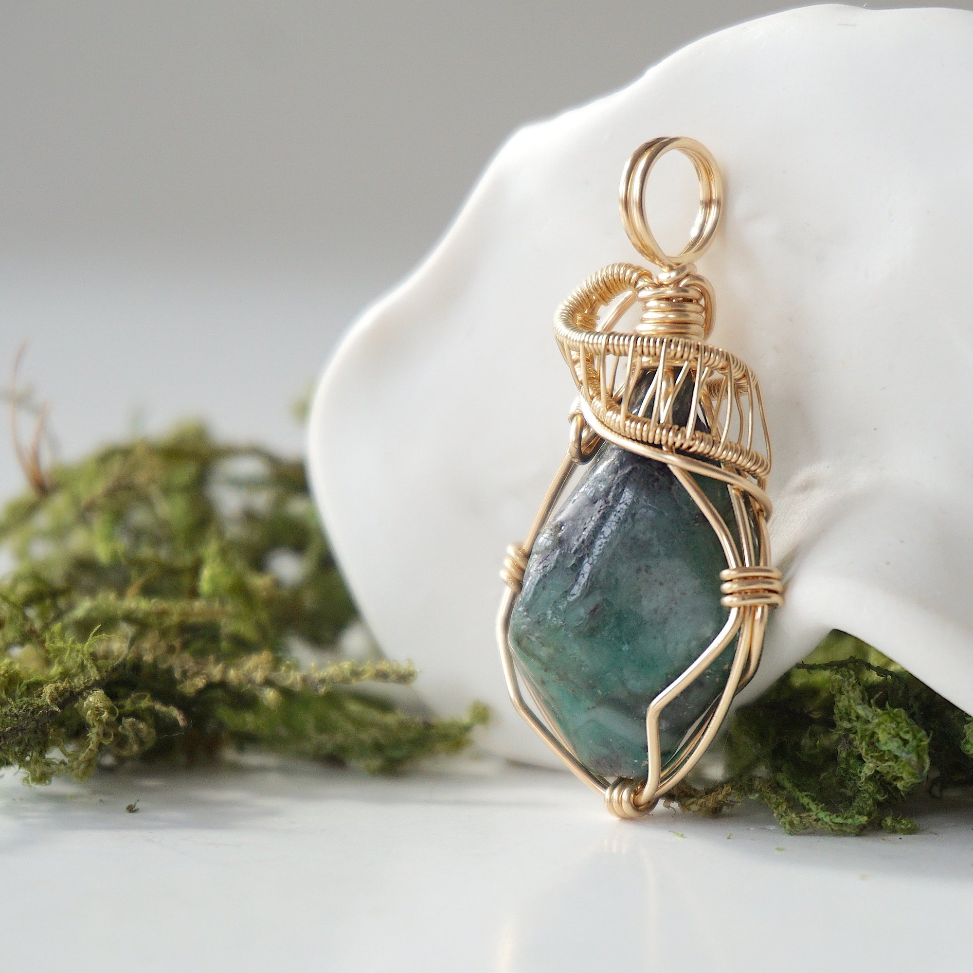Side angle detail of natural emerald pendant highlighting intricate artisan wrapping in 14k gold-filled wire.