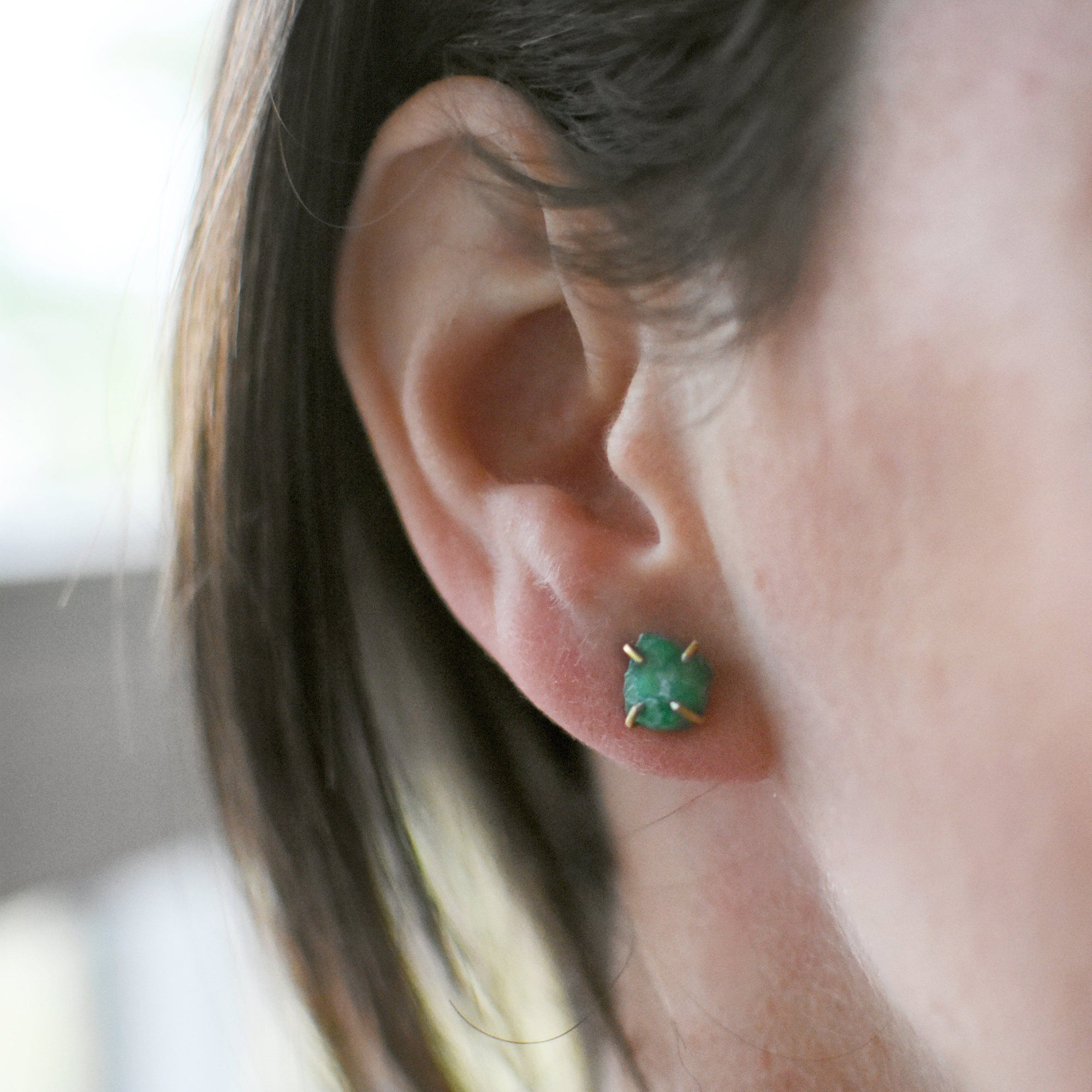 Female model wearing raw emerald stud earrings in 14k gold vermeil with natural emerald stones and minimalist design