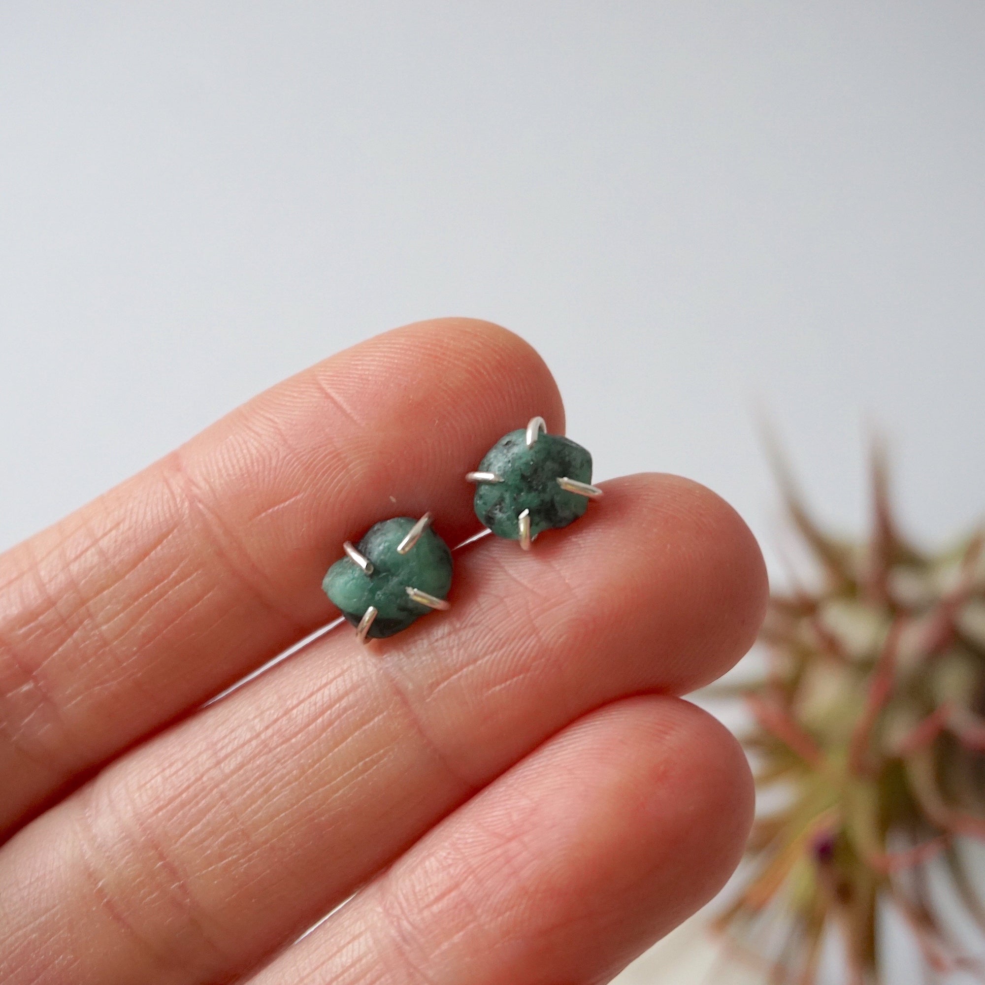 Natural raw emerald stud earrings in sterling silver shown in hand to display size and organic stone variation