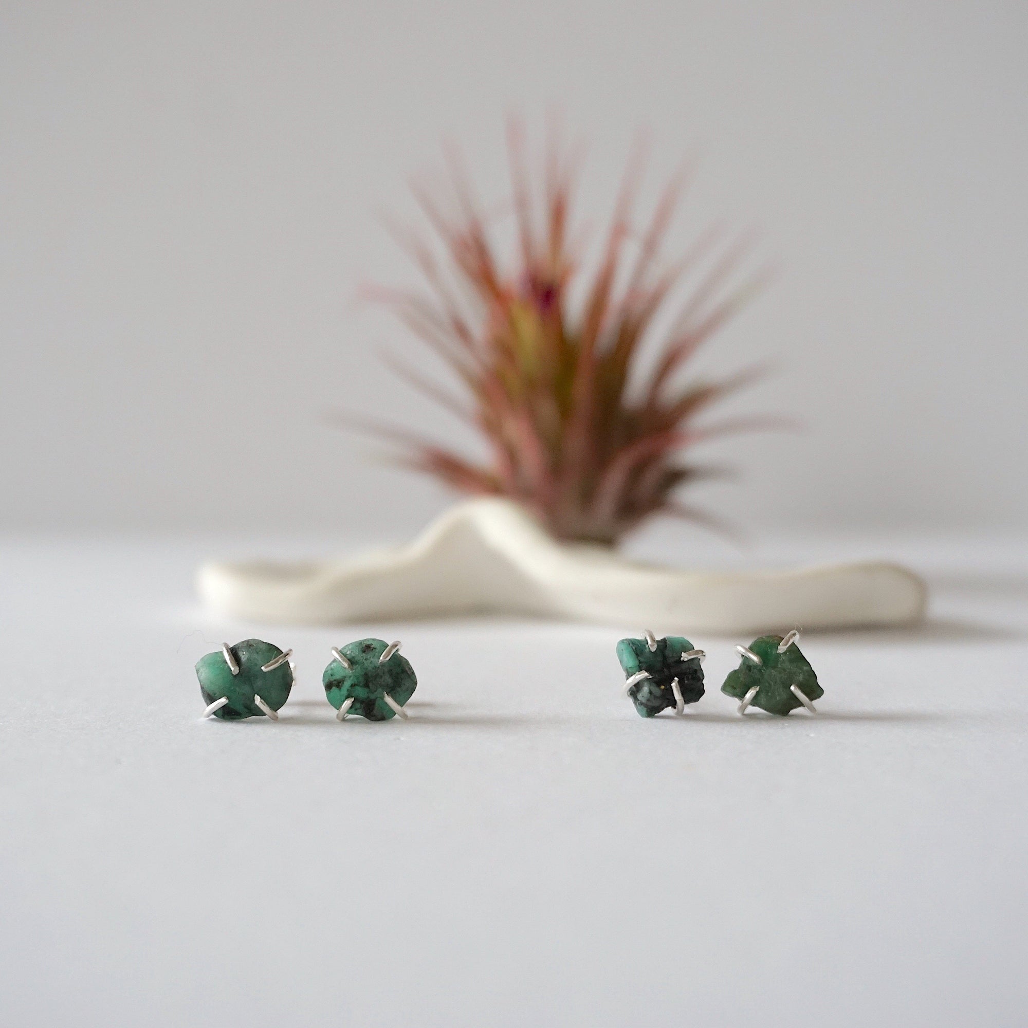 Two pairs of raw emerald stud earrings in sterling silver showing natural variation in emerald shape size and green colour