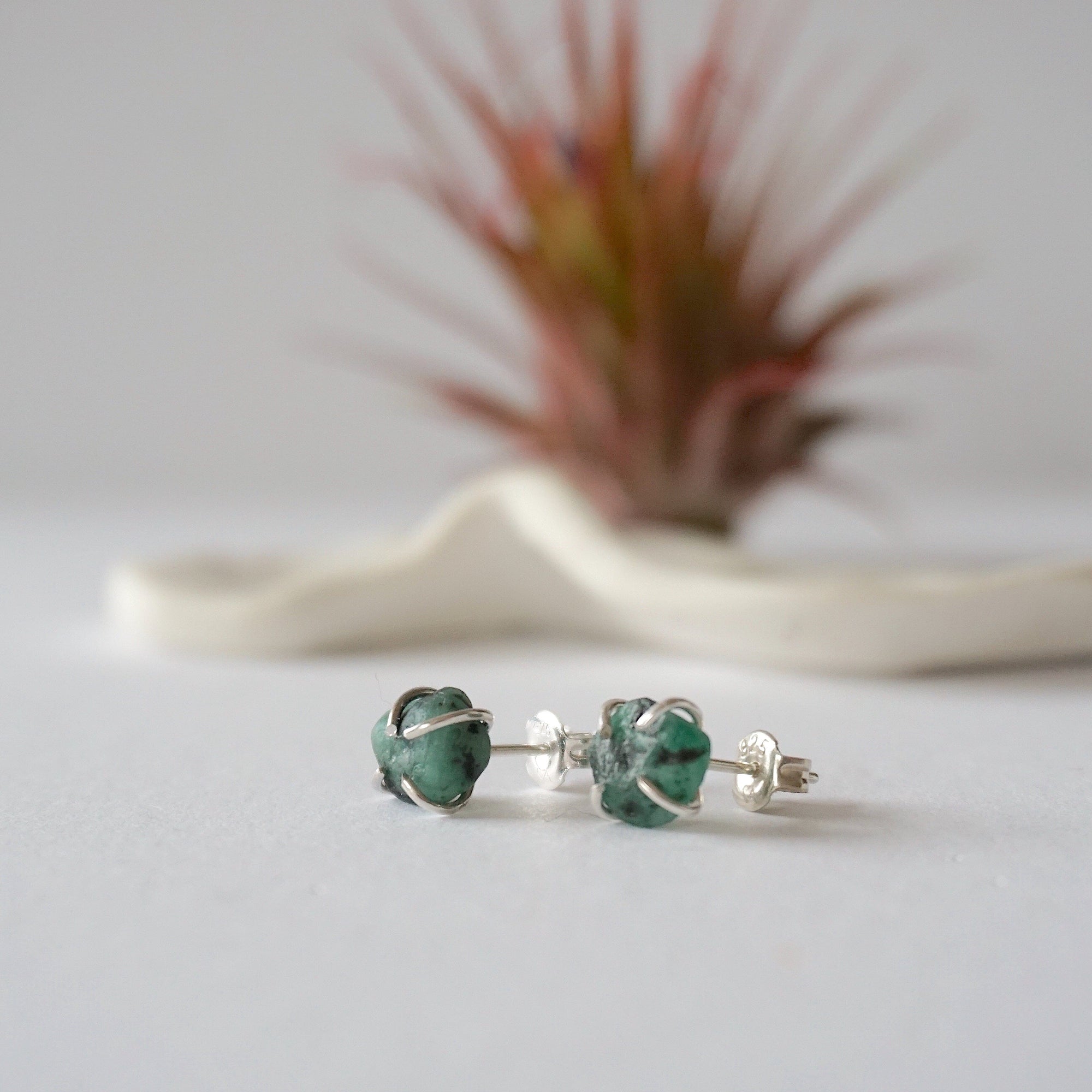Raw emerald stud earrings in sterling silver at a slight angle showing natural green emerald and minimalist prong setting