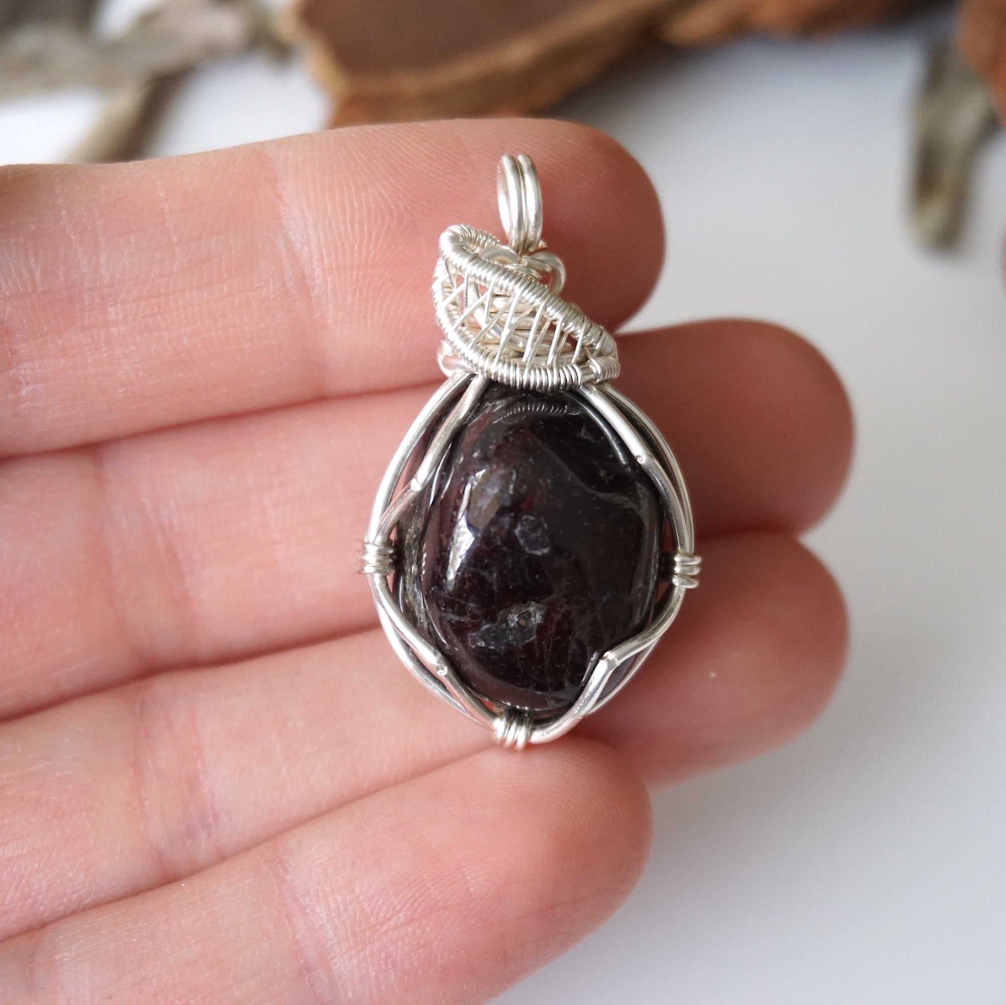 Raw garnet pendant necklace held in hand for size reference, detailed silver plated copper wire wrap