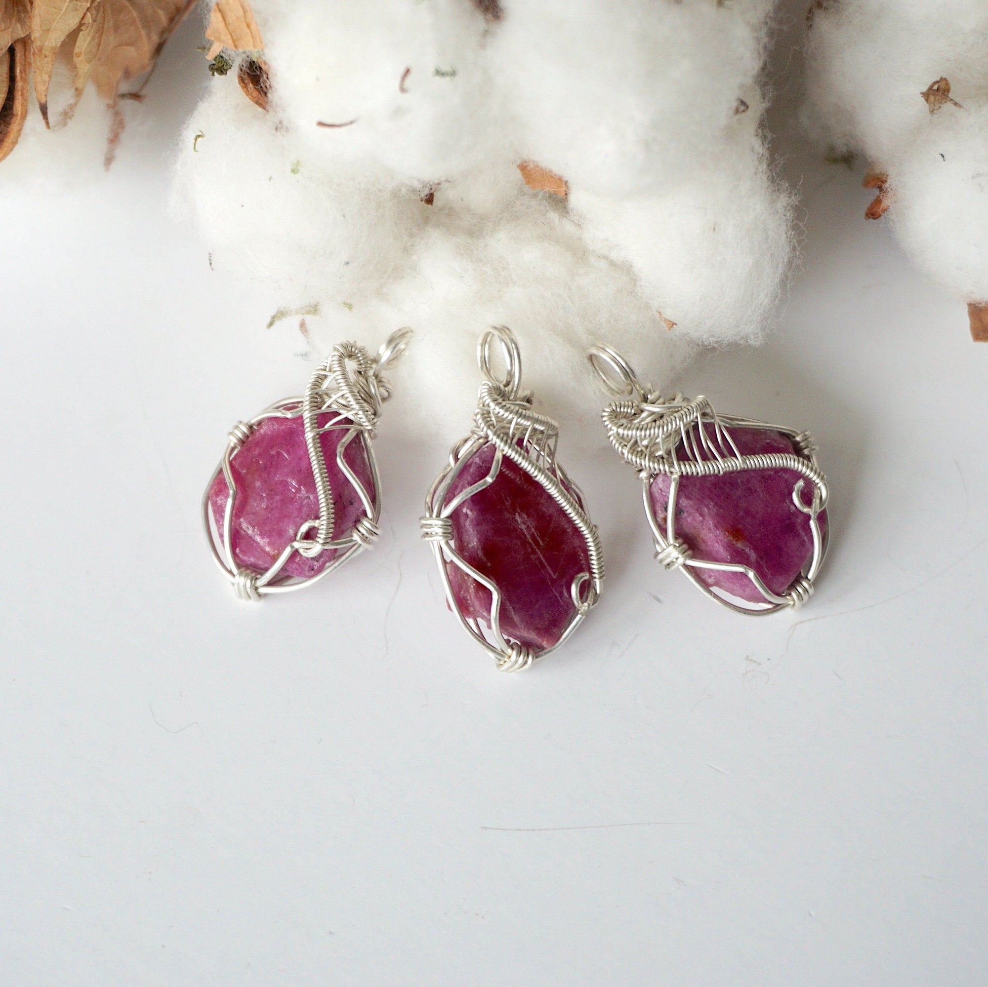Three raw ruby pendants showing natural variation in color, size, and shape, sterling silver artisan wire wrapped