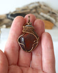 Natural red tiger's eye pendant in hand for size reference, handcrafted by Designs by Nature Gems.