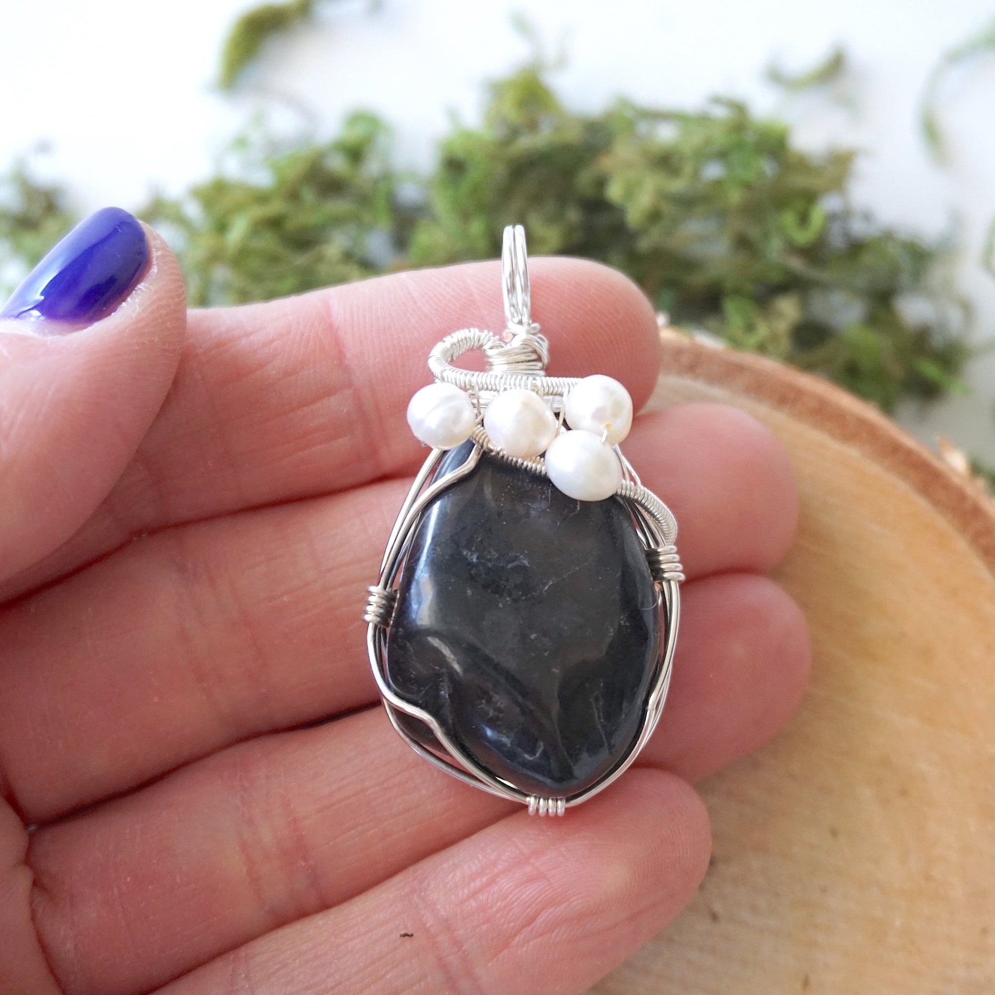 Shungite and freshwater pearl pendant necklace in hand for size reference, silver wire wrapped, handcrafted gemstone jewelry