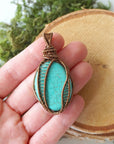 Turquoise pendant necklace held in hand showing size reference and scale of natural stone with bronze wire wrapping