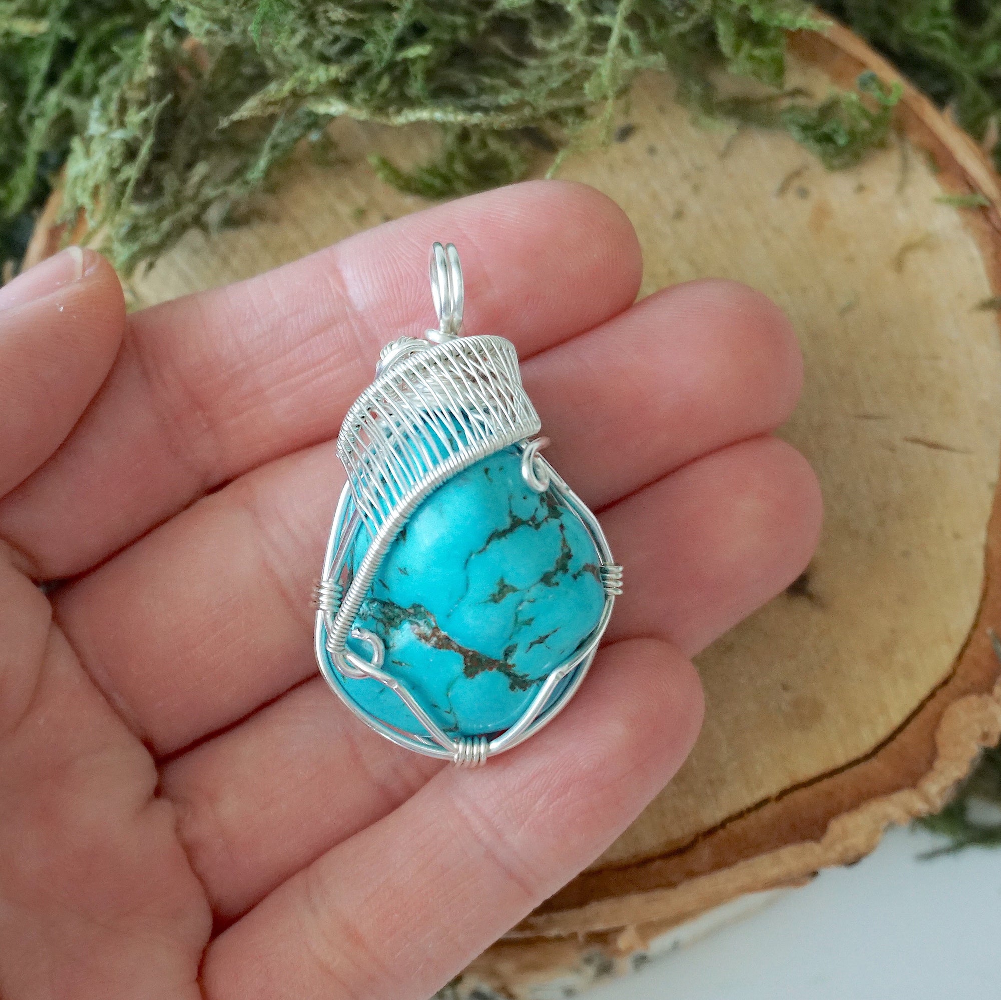 Raw turquoise pendant size in hand showing silver wire wrap detail