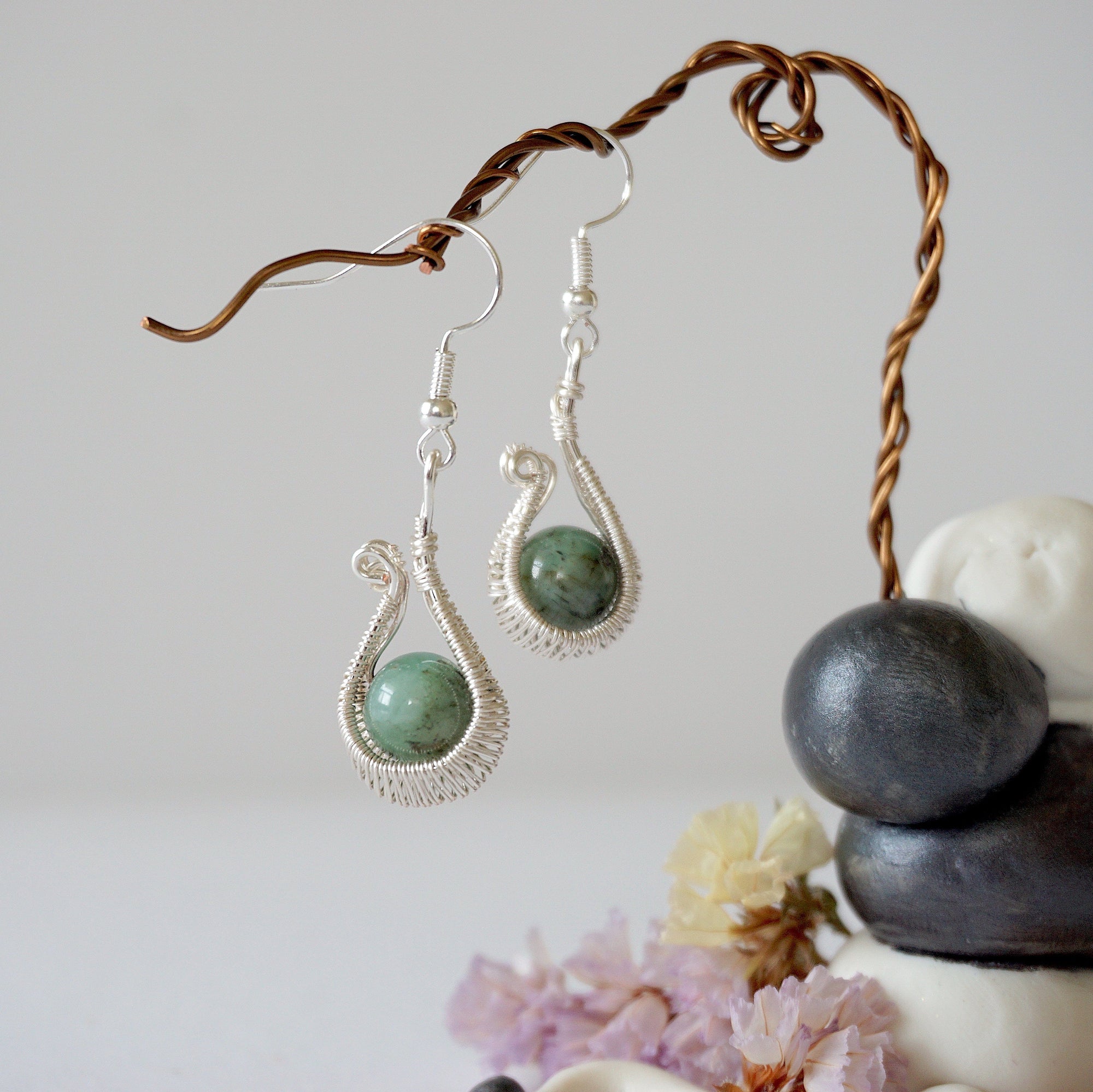 Close detail of wire wrapped emerald drop earrings showing intricate artisan wrapping around natural emerald bead