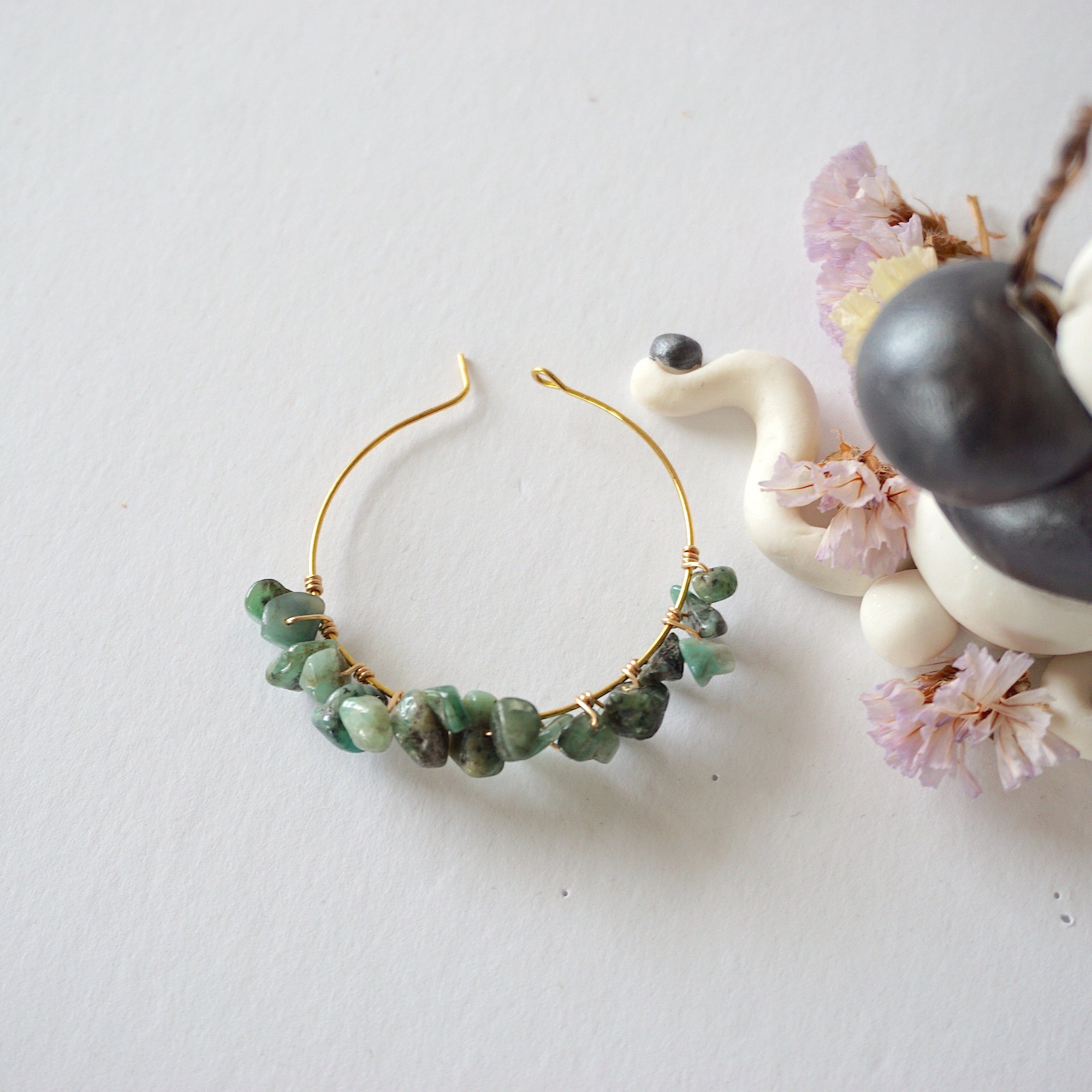 Emerald hoop earrings on flat surface showing classic hoop shape natural emerald chips and handcrafted wire wrapping