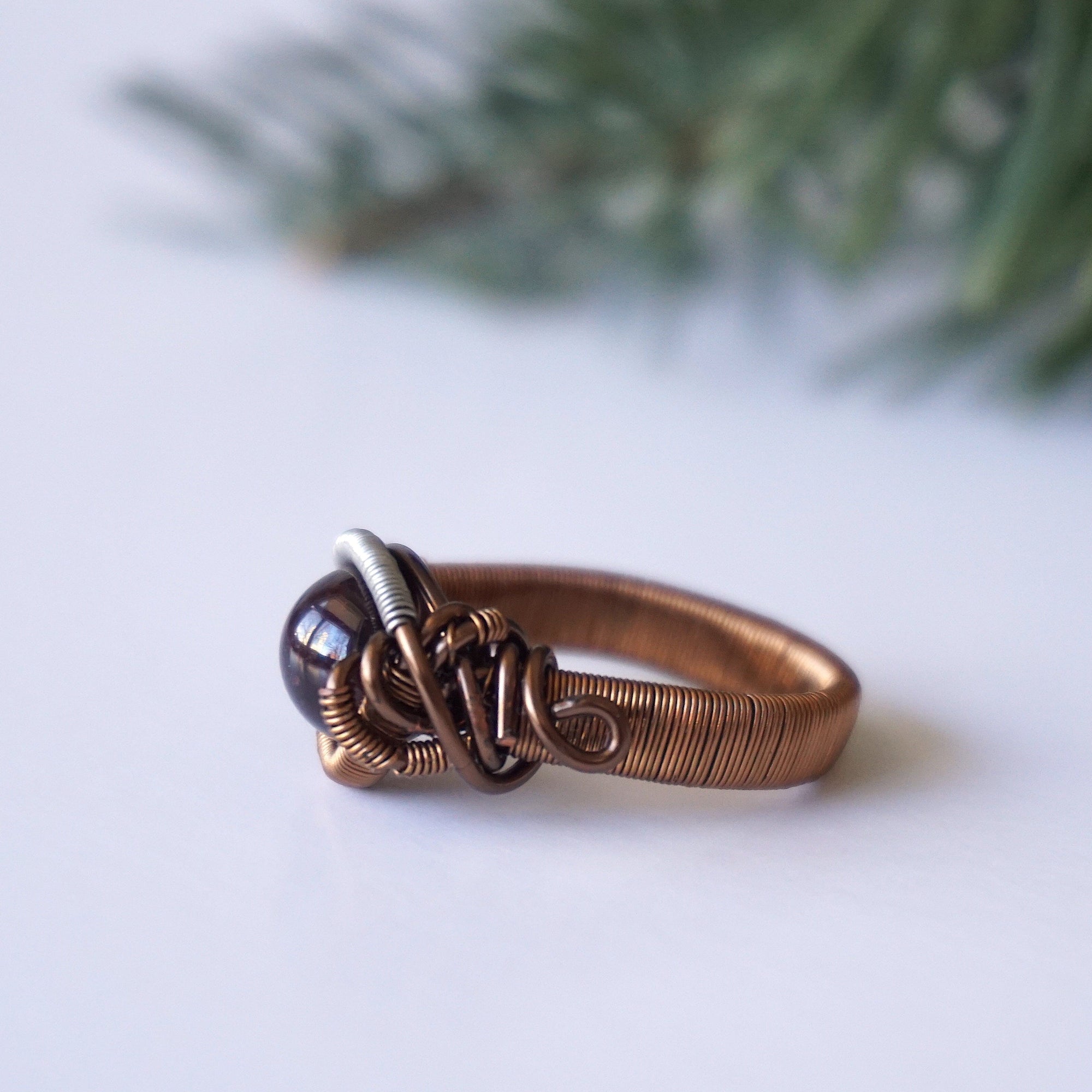 Left side angle view of a gender neutral wire wrapped garnet ring in antique bronze and tin-plated copper