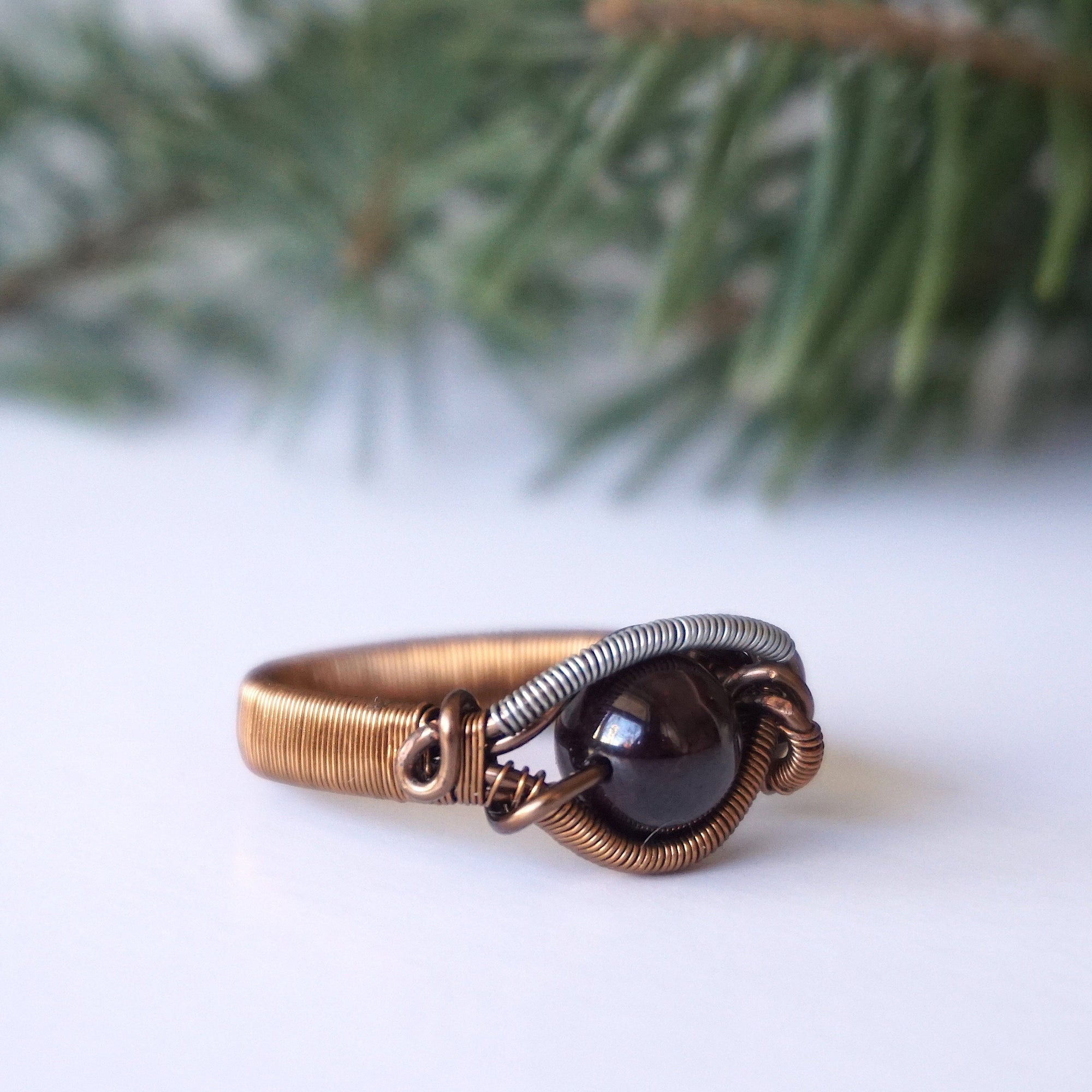 Right side angle view of a wire wrapped garnet ring highlighting the geometric mixed metal wire pattern