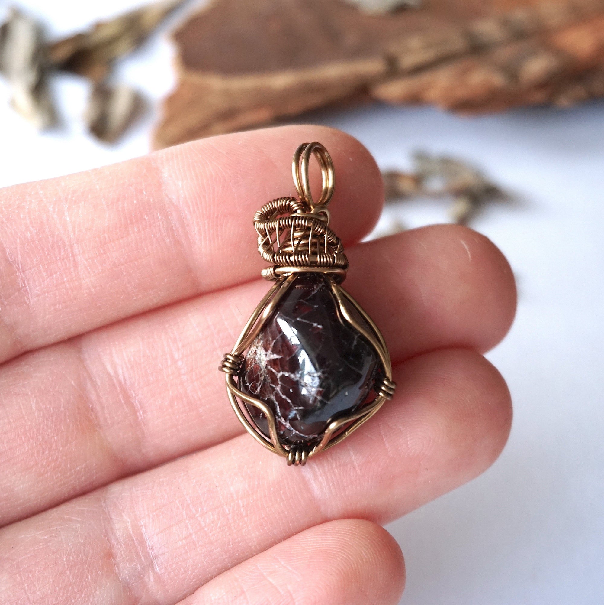 Women’s garnet pendant necklace in antique bronze copper held in hand for size reference, featuring a natural deep red garnet stone
