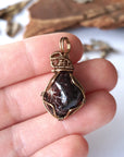 Women’s garnet pendant necklace in antique bronze copper held in hand for size reference, featuring a natural deep red garnet stone