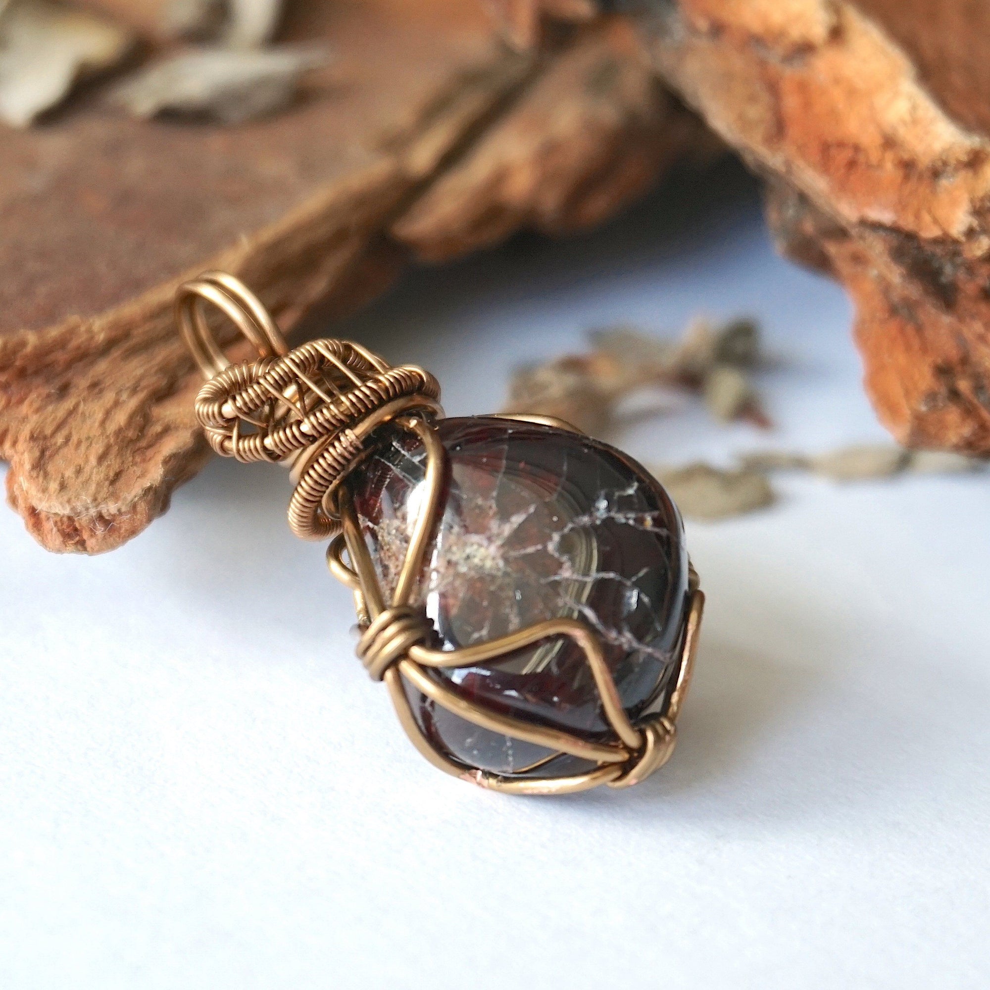 Side angle view of a women’s garnet wire wrapped necklace, highlighting the antique bronze copper wrap and gemstone profile