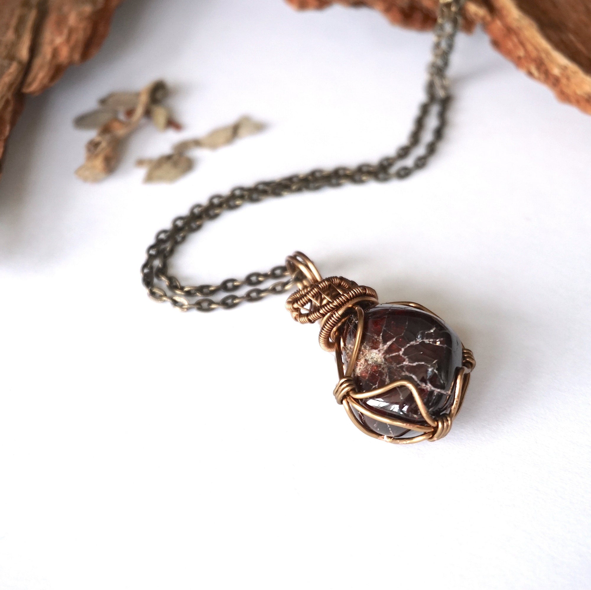 Women’s garnet wire wrapped necklace in antique bronze copper on an antique bronze chain, shown laying flat to highlight the natural garnet pendant